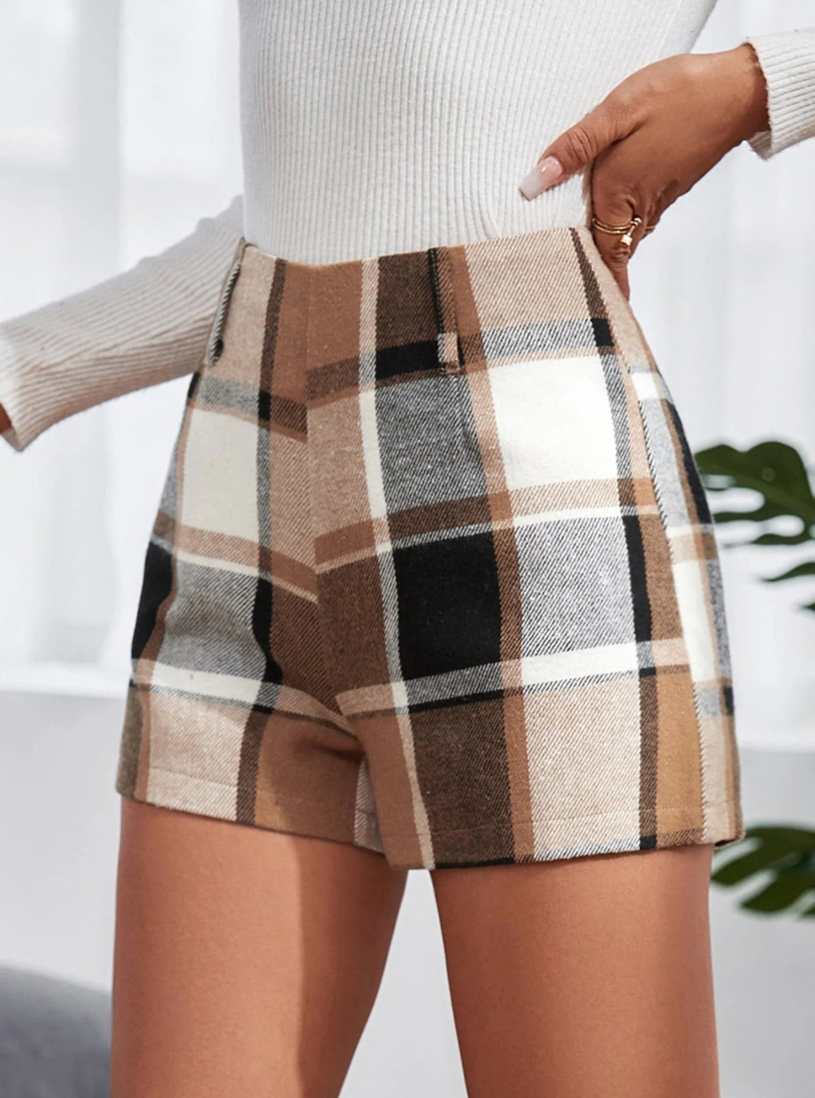 Plaid shorts worn with a white sweater against a neutral background