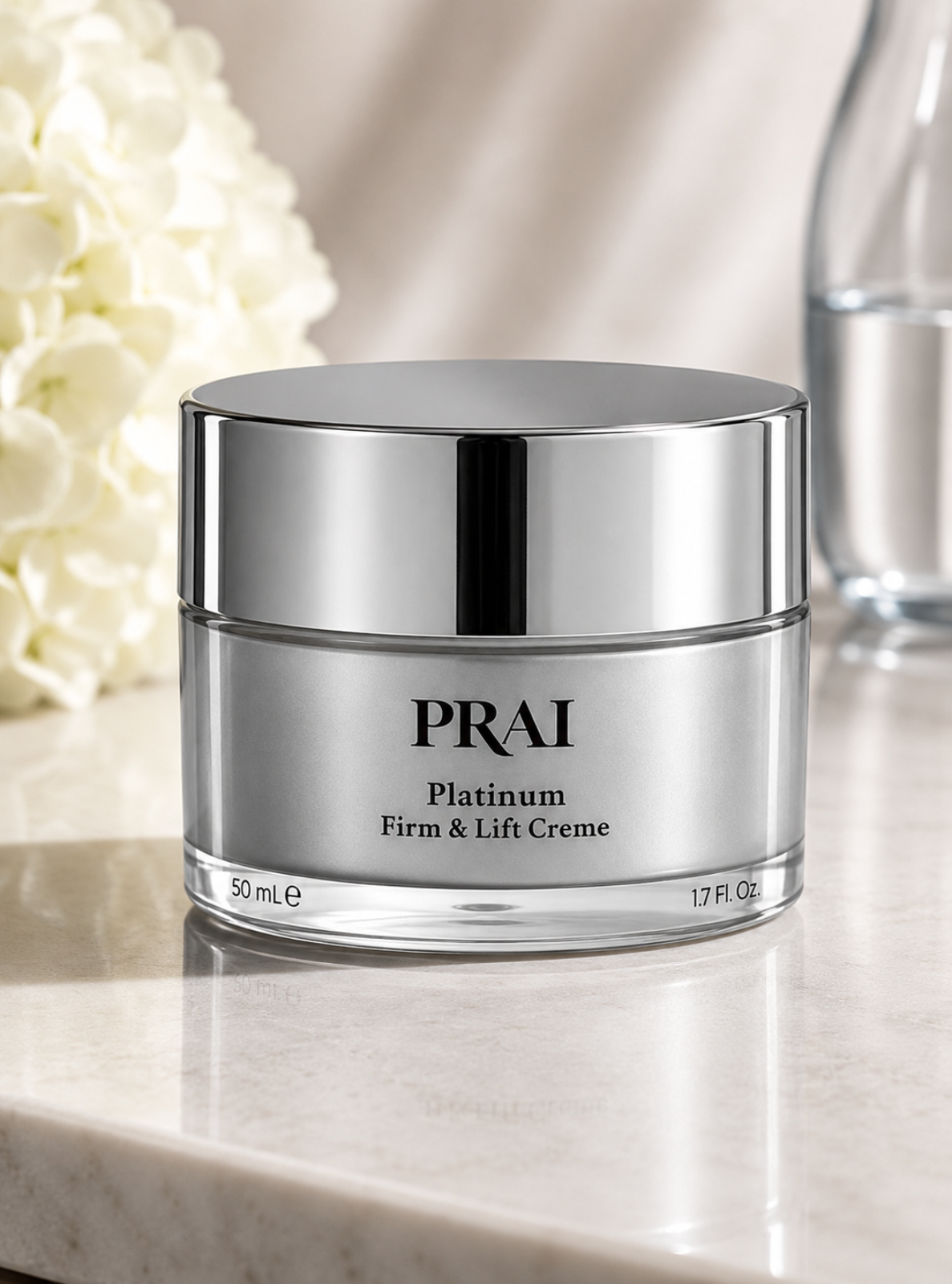 A silver jar of PRAI Platinum Firm & Lift Creme on a light marble surface with soft-focus white flowers and a glass bottle in the background.