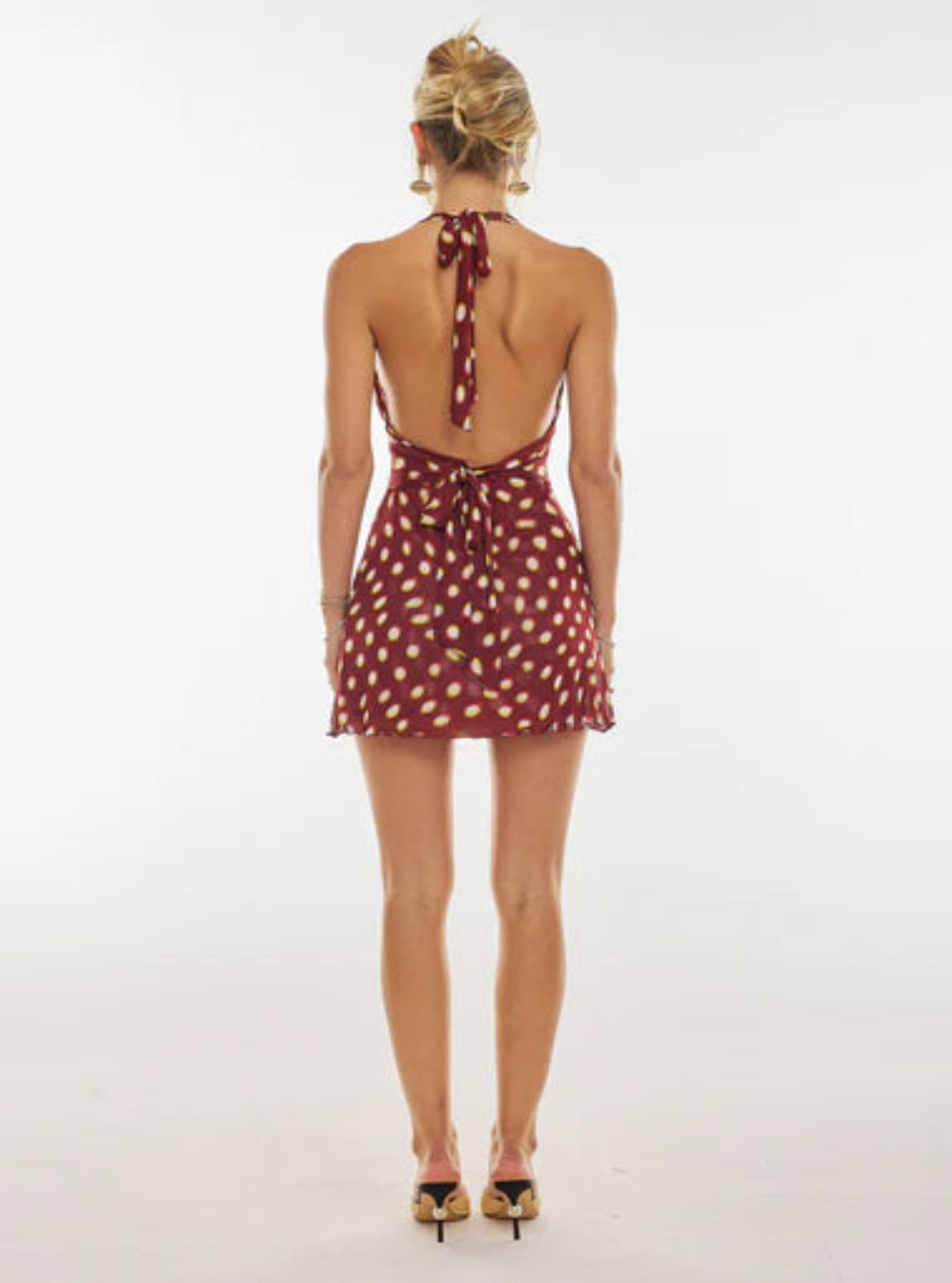 Woman wearing a red polka dot dress with a back tie on a white background