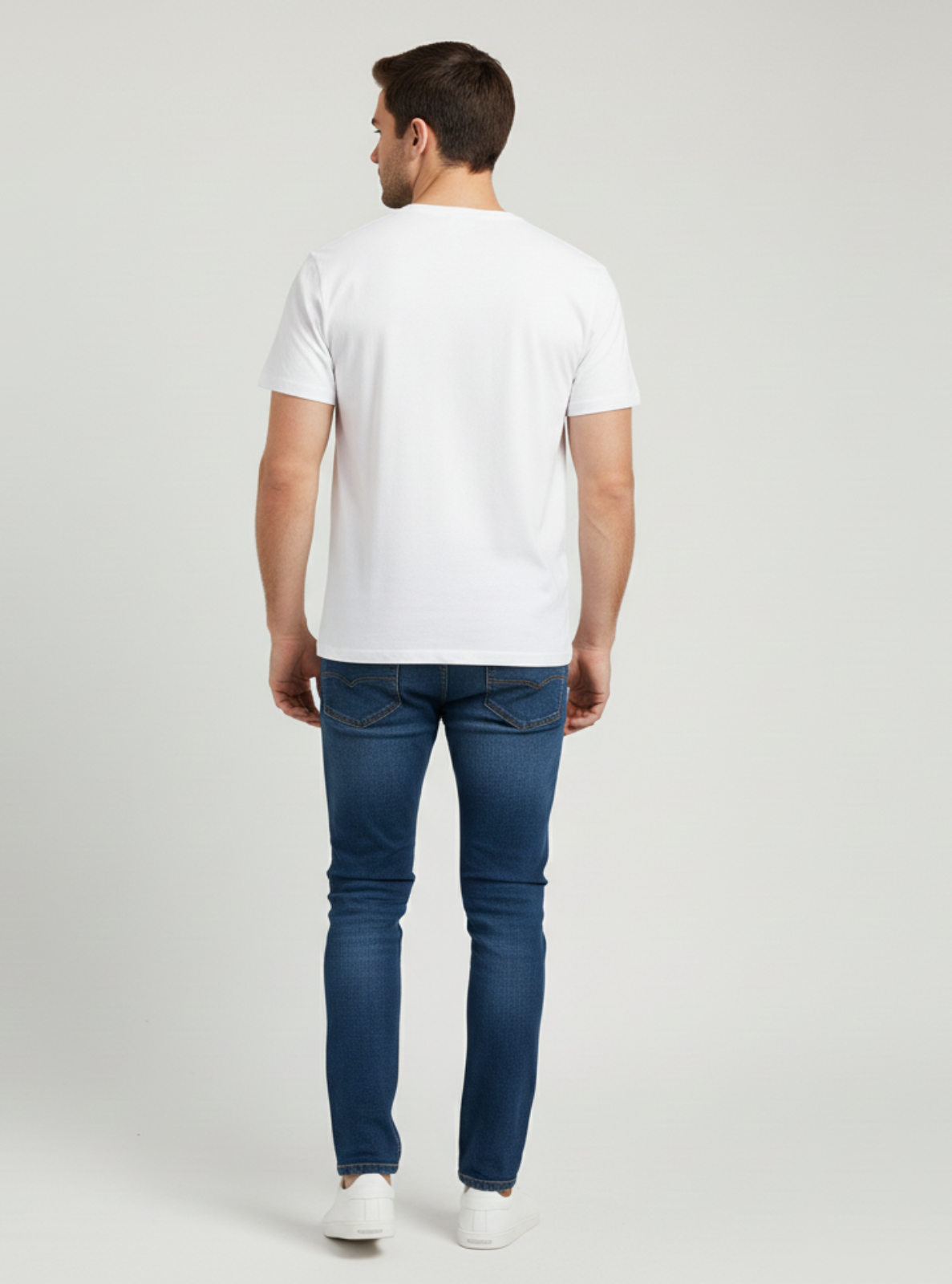 Man wearing a white t-shirt and blue jeans on a light gray background