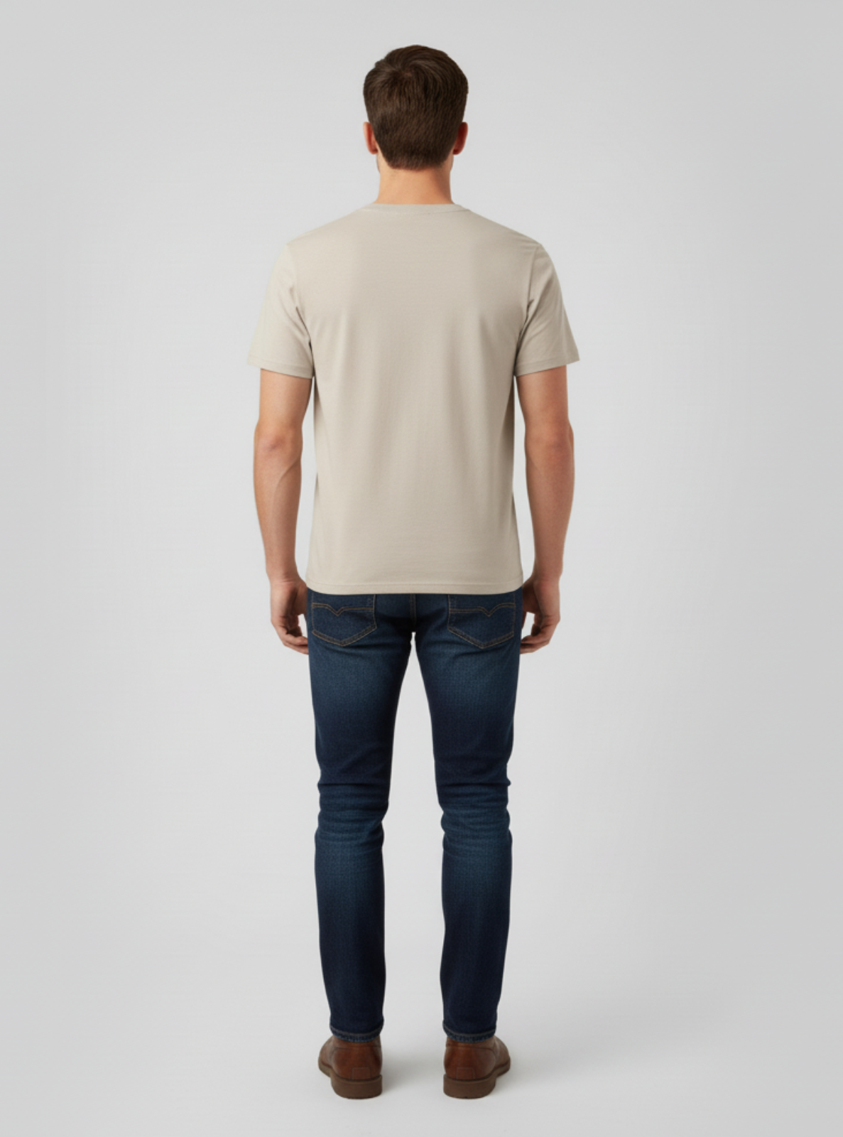 Man wearing a beige t-shirt and dark jeans on a light gray background