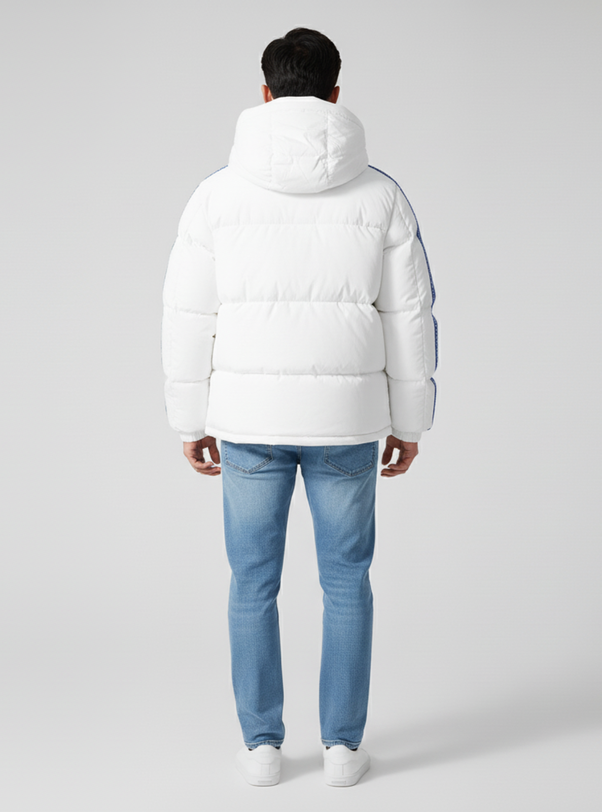 Person wearing a white puffer jacket and blue jeans on a gray background