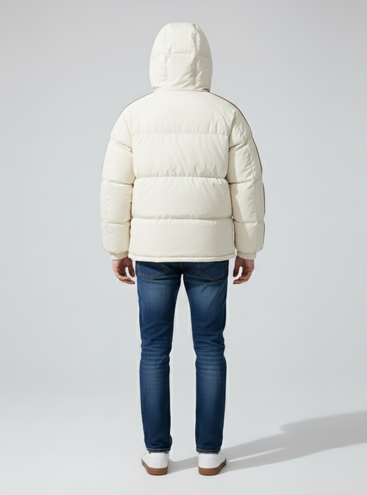 Person wearing a white puffer jacket and blue jeans on a light gray background