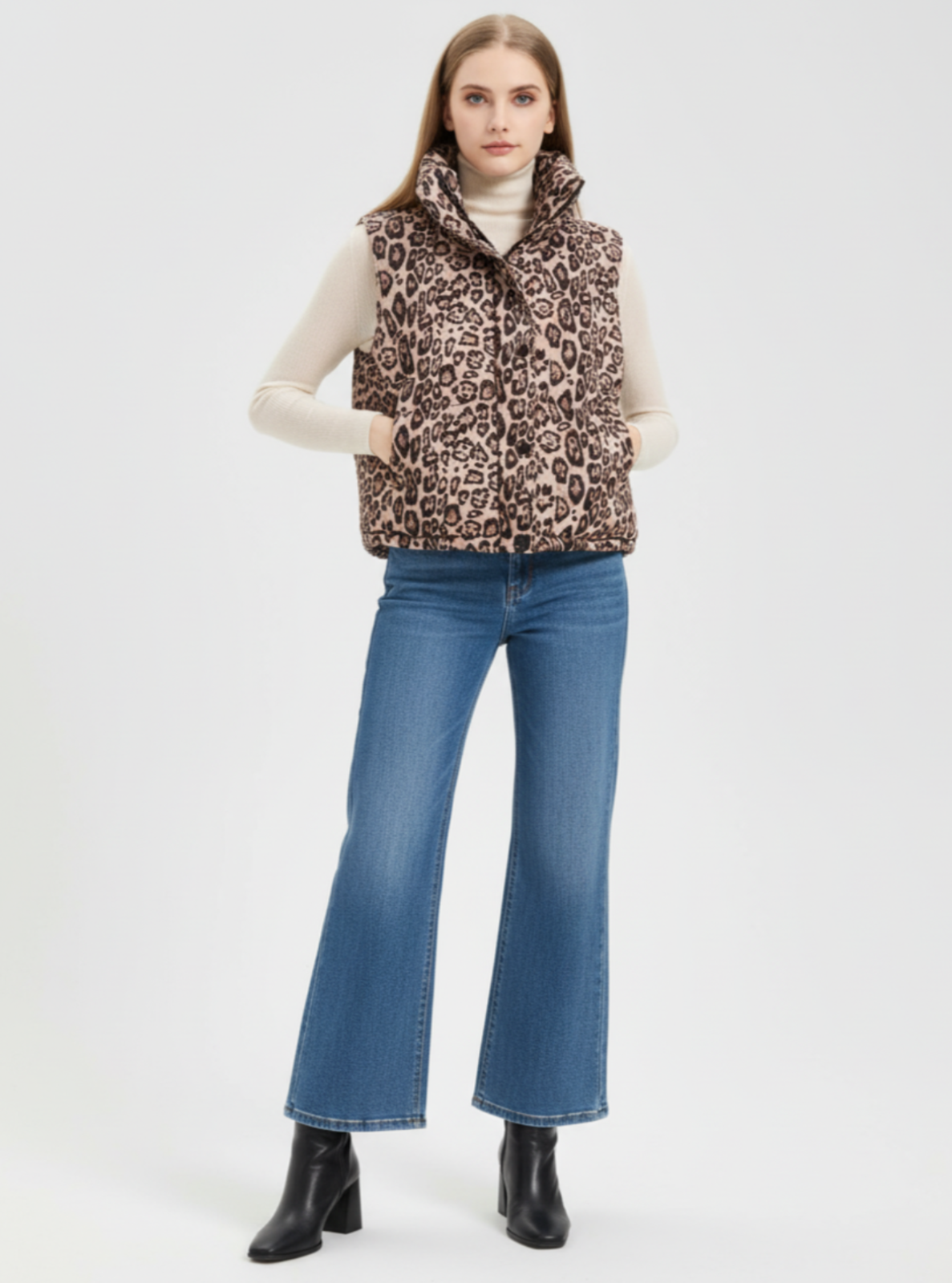 Woman wearing a leopard print puffer vest, white turtleneck, blue jeans, and black boots on a white background