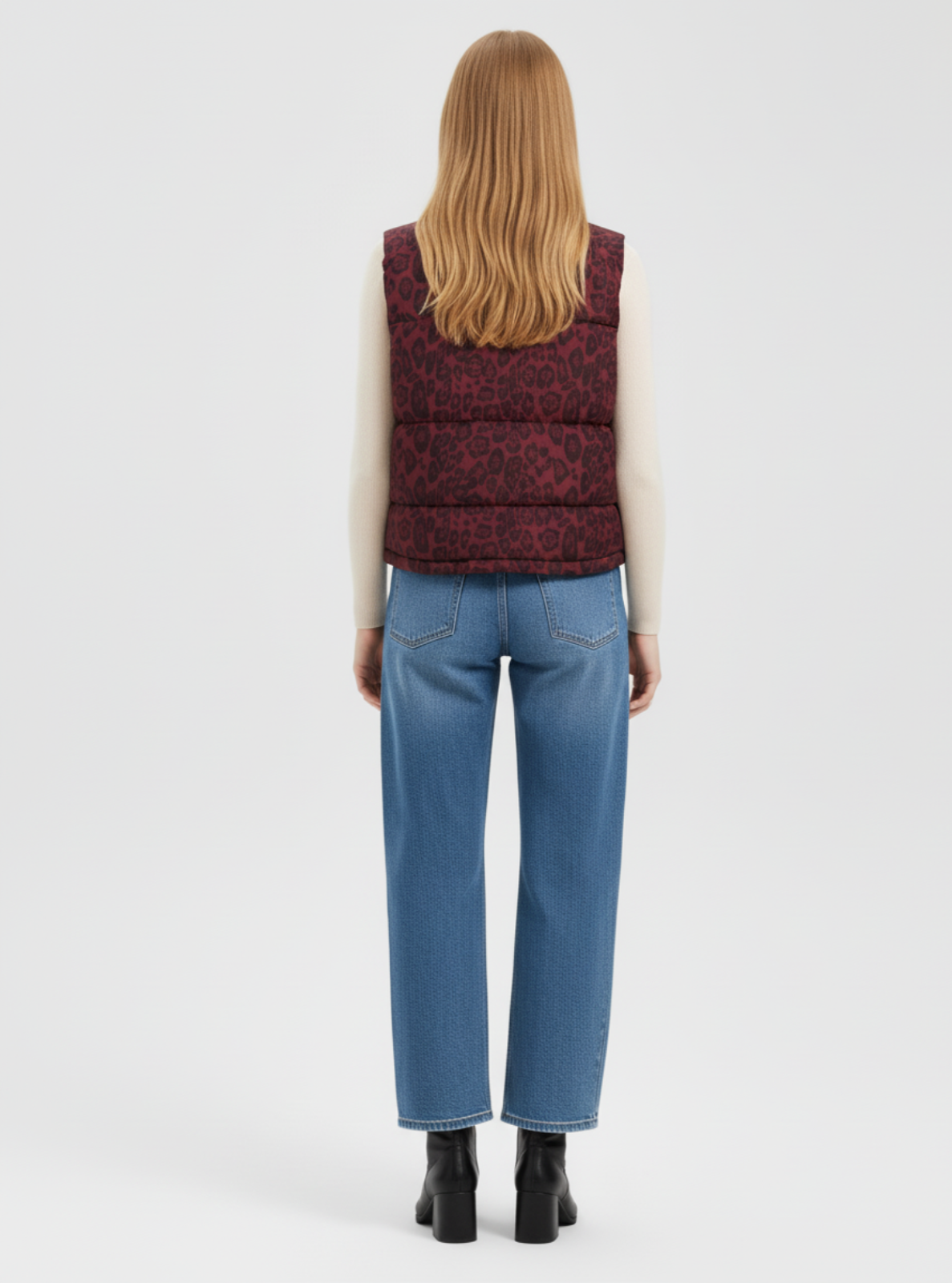 Person wearing a patterned vest and blue jeans from behind on a white background