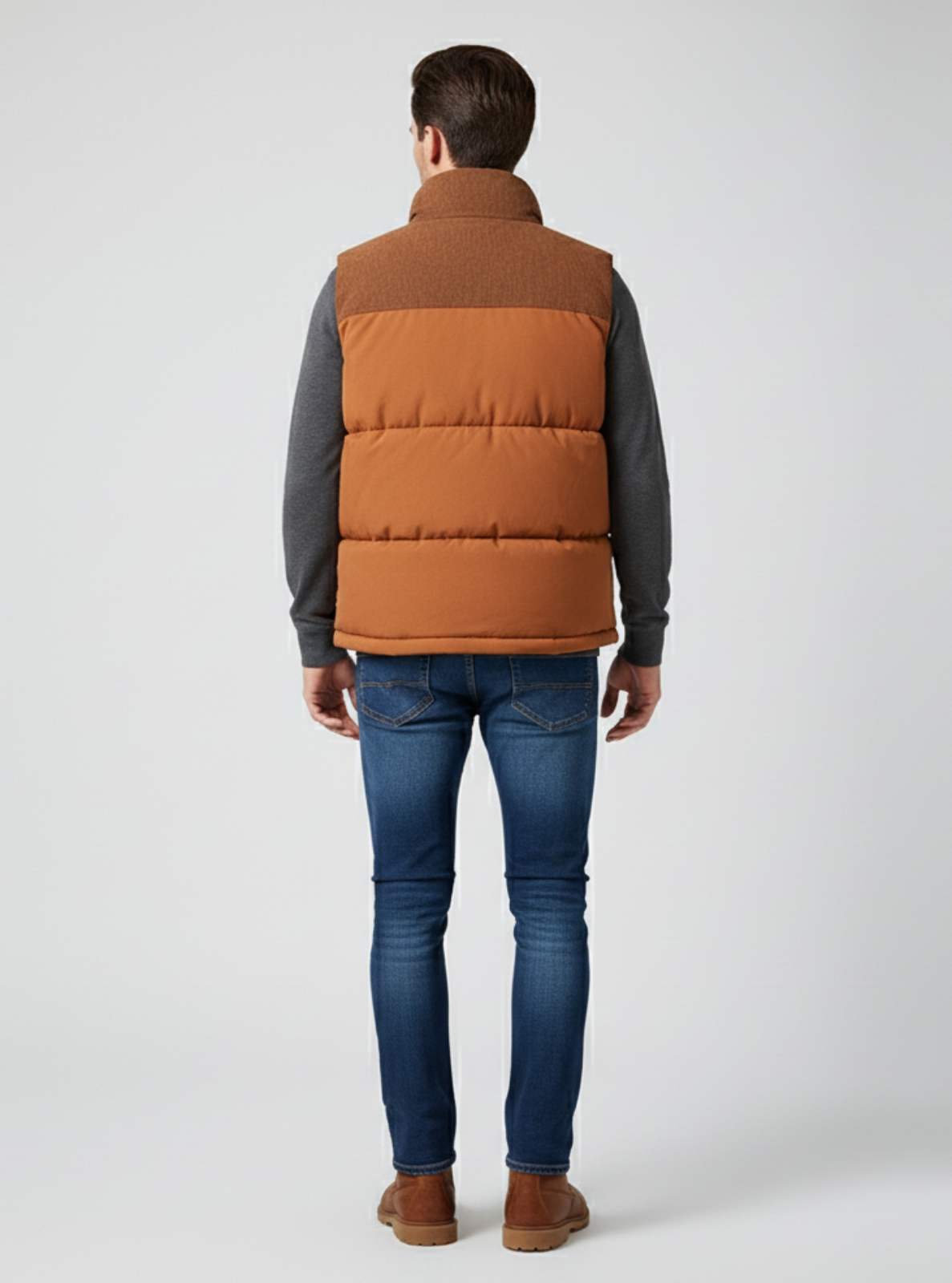 Man wearing a brown puffer vest over a gray shirt with blue jeans on a white background