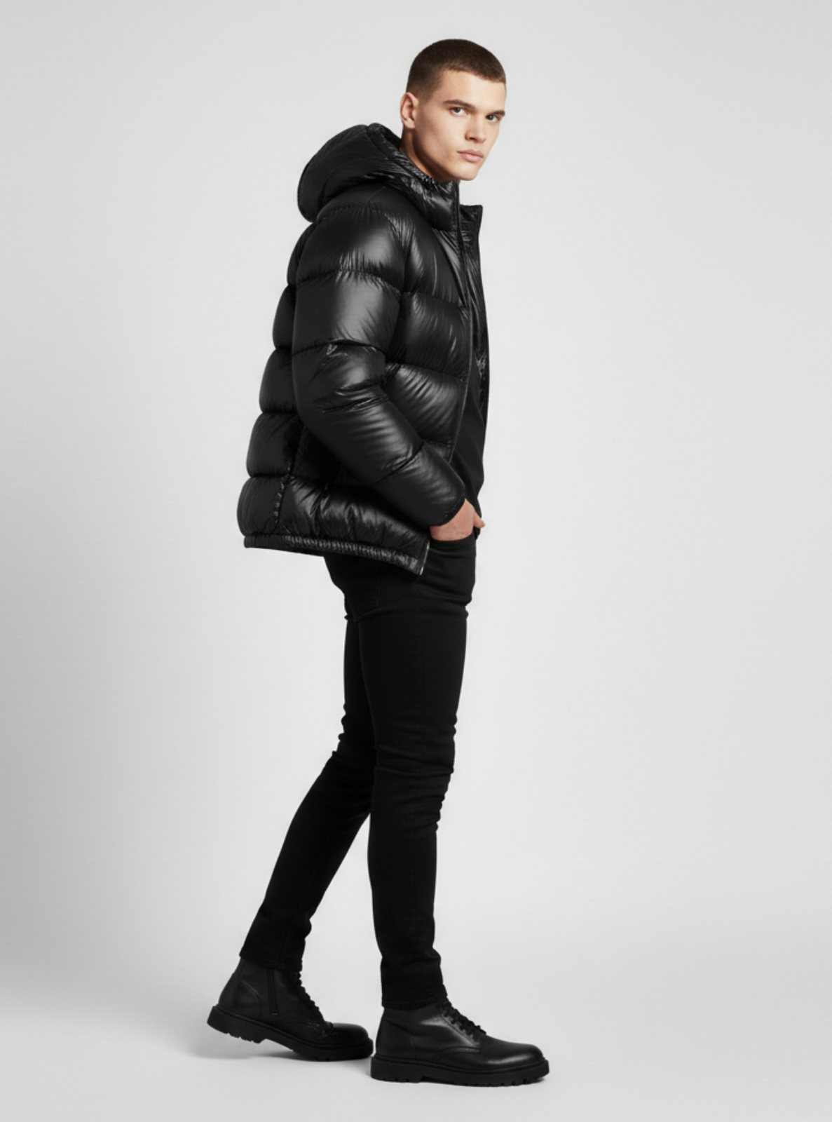 Man wearing a black puffer jacket and black pants on a gray background