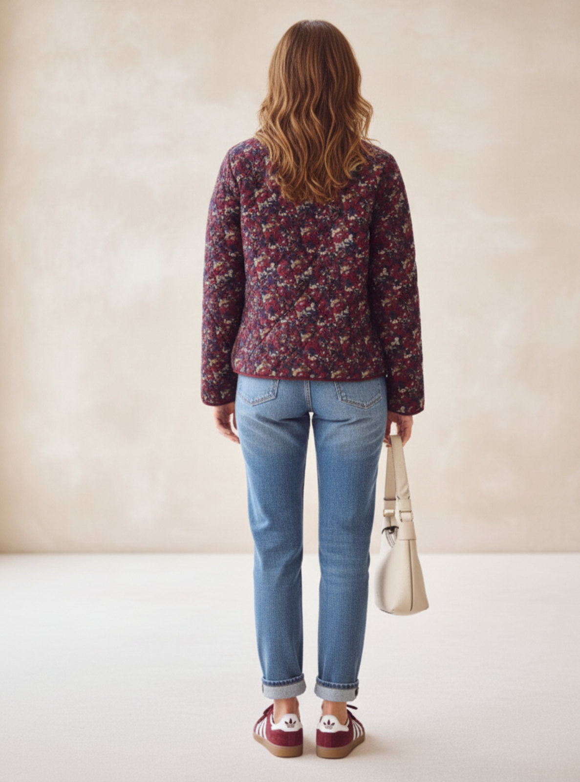 Woman wearing a floral blouse and blue jeans, standing against a plain background