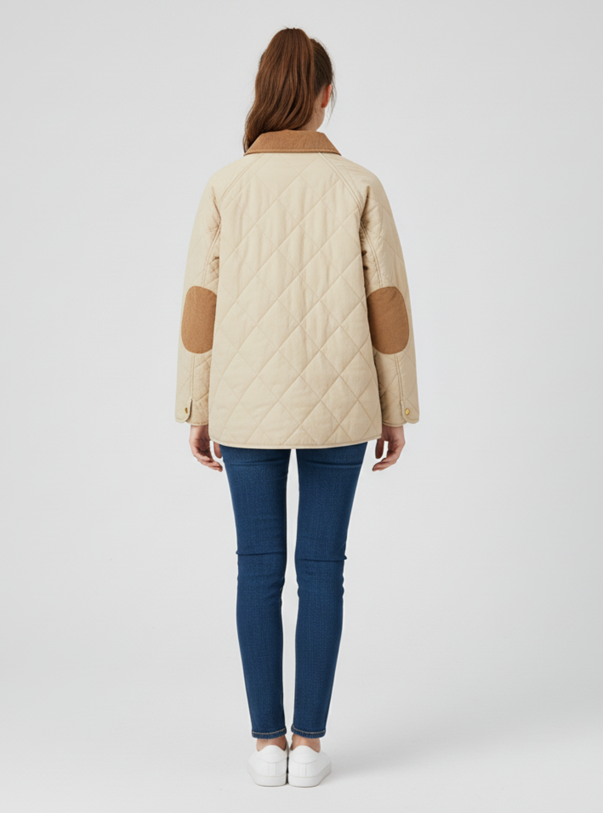 Woman wearing a beige quilted jacket with brown elbow patches on a white background