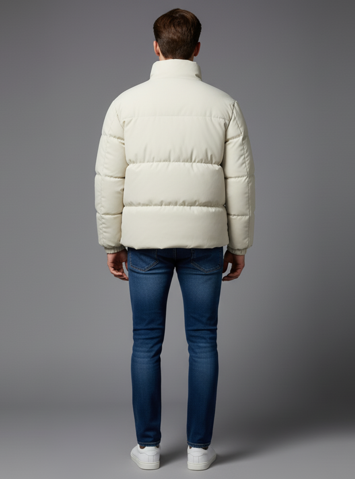 Person wearing a white puffer jacket and blue jeans on a gray background