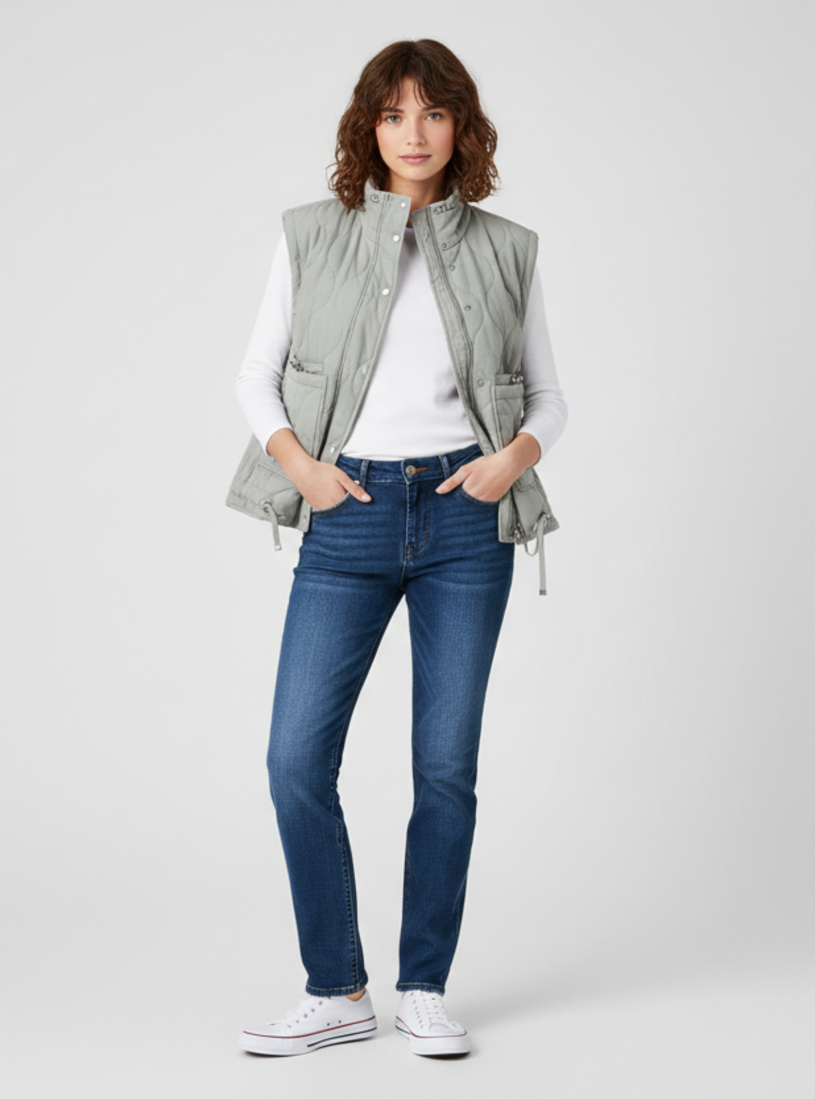 Woman wearing a gray vest over a white shirt with blue jeans on a white background