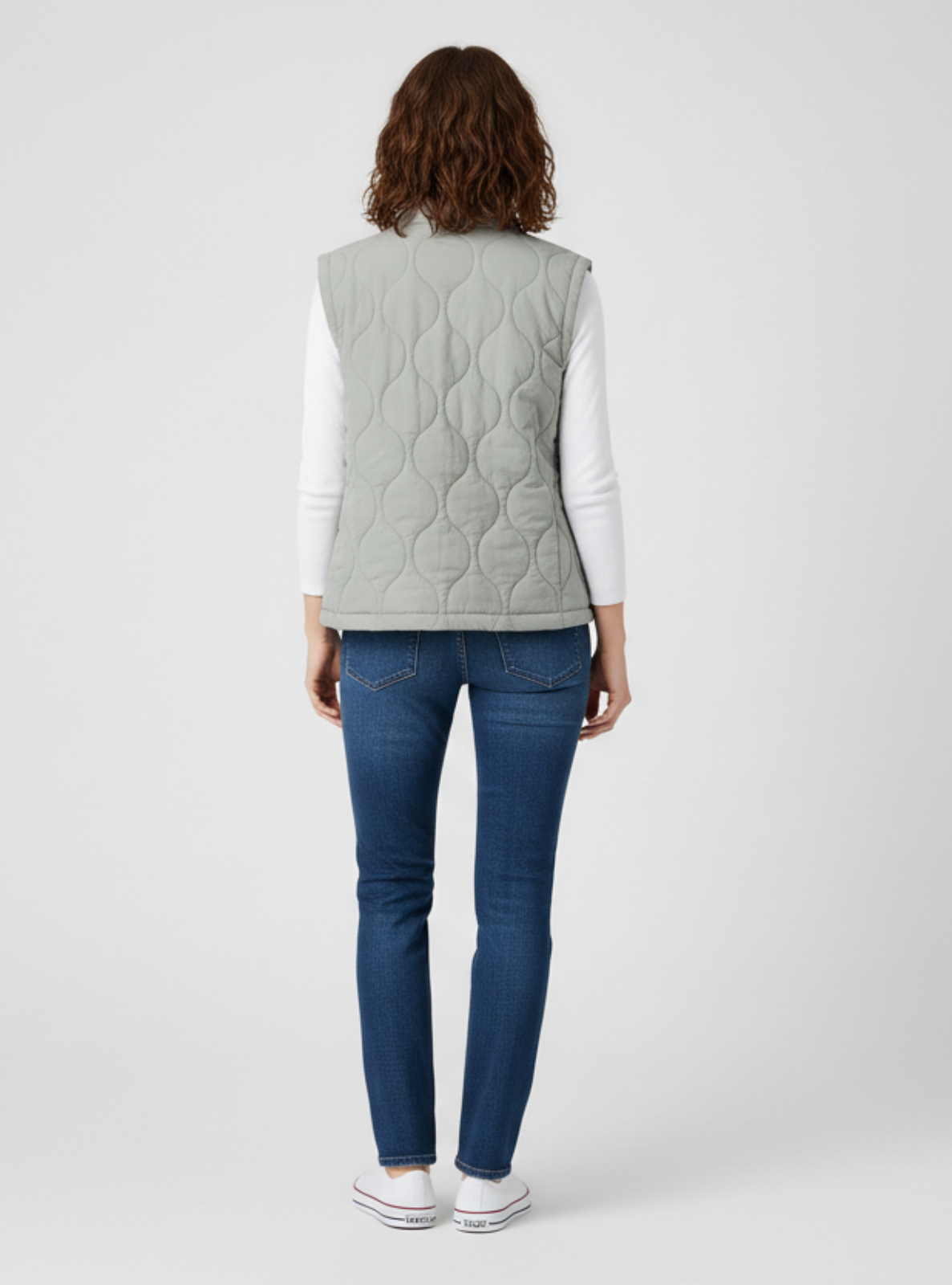 Person wearing a light gray quilted vest and blue jeans on a white background