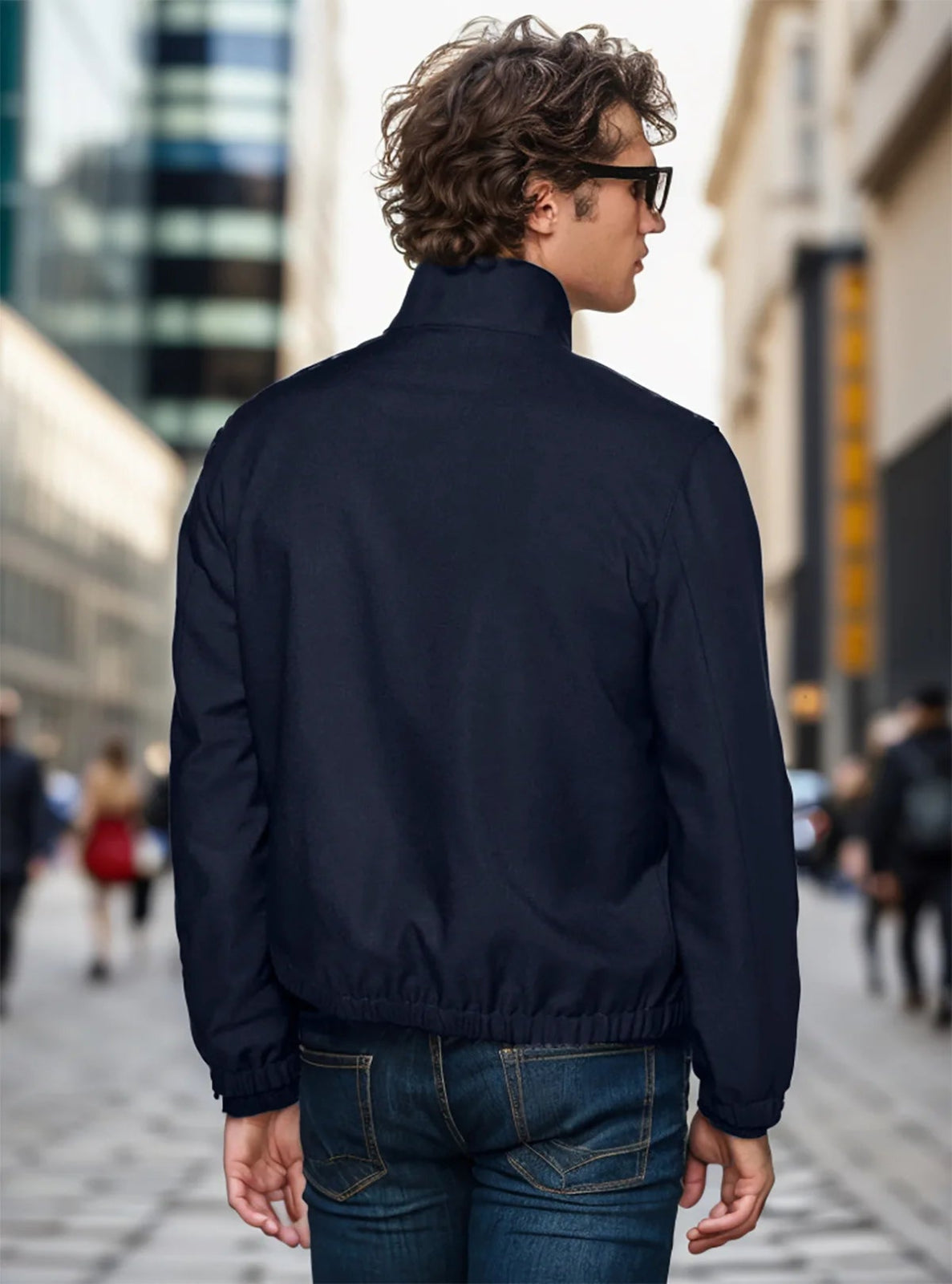Person wearing a dark blue jacket and sunglasses on a city street.