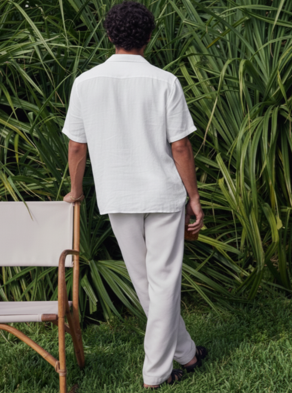 Man in light-colored shirt and pants standing in a garden with greenery.