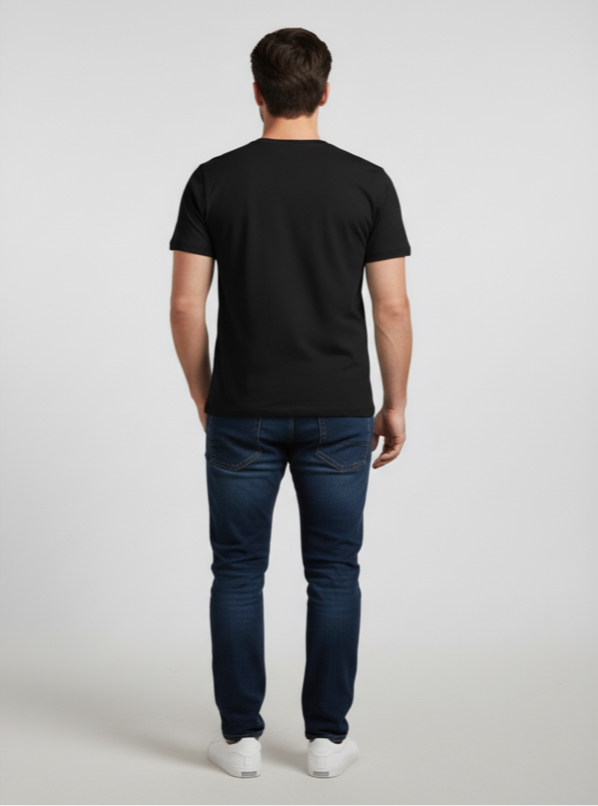 Man wearing a black t-shirt and dark jeans on a light gray background