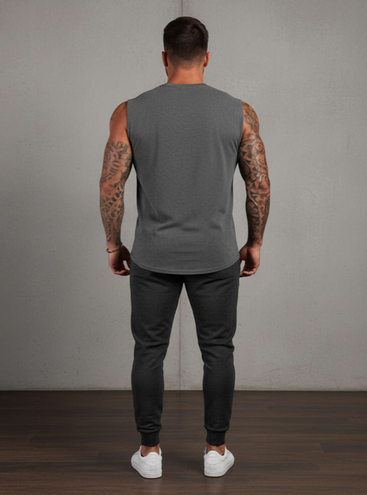 Man wearing a gray sleeveless shirt and dark pants against a plain background