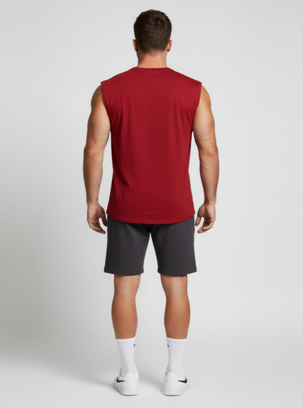Man wearing a red sleeveless shirt and gray shorts on a white background