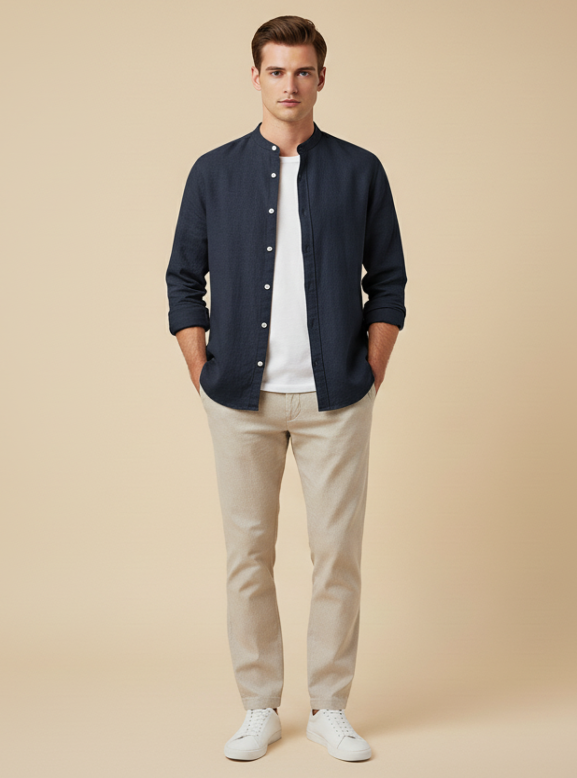 Man wearing a navy button-up shirt, white t-shirt, beige pants, and white sneakers on a beige background