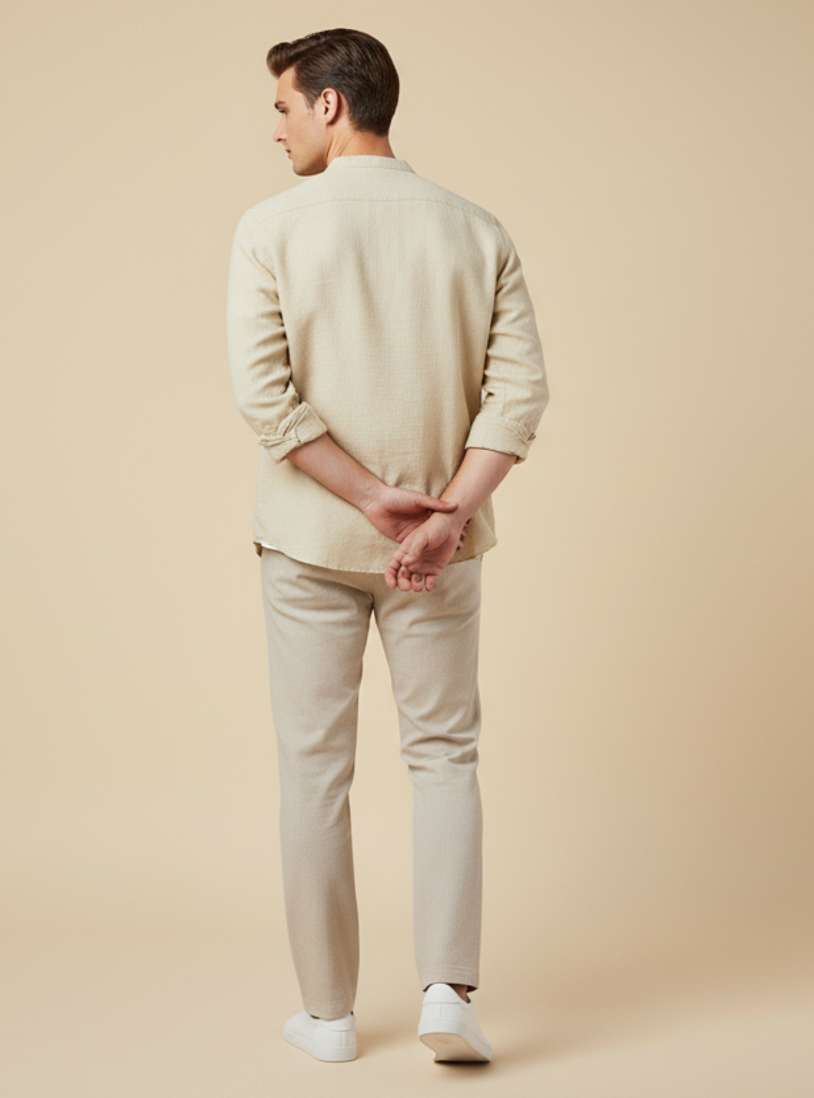 Man wearing a beige sweater and pants standing against a beige background