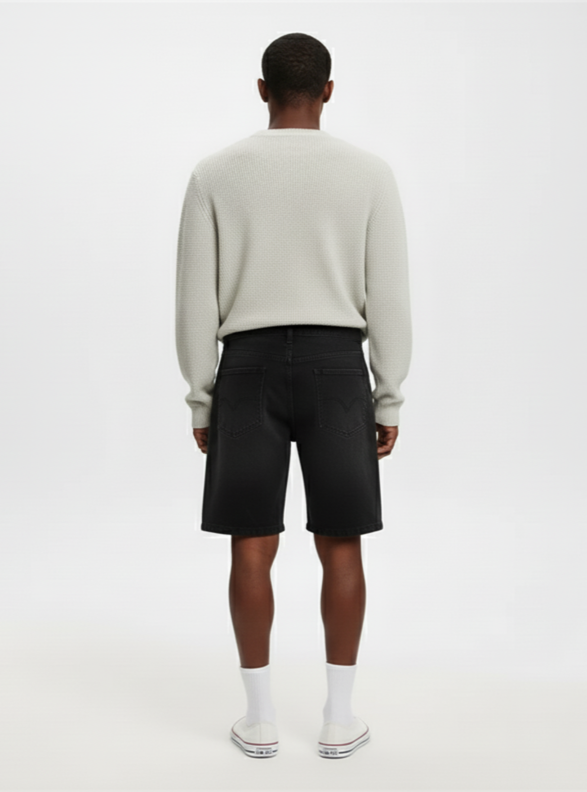 Person wearing a light gray sweater and black shorts on a white background
