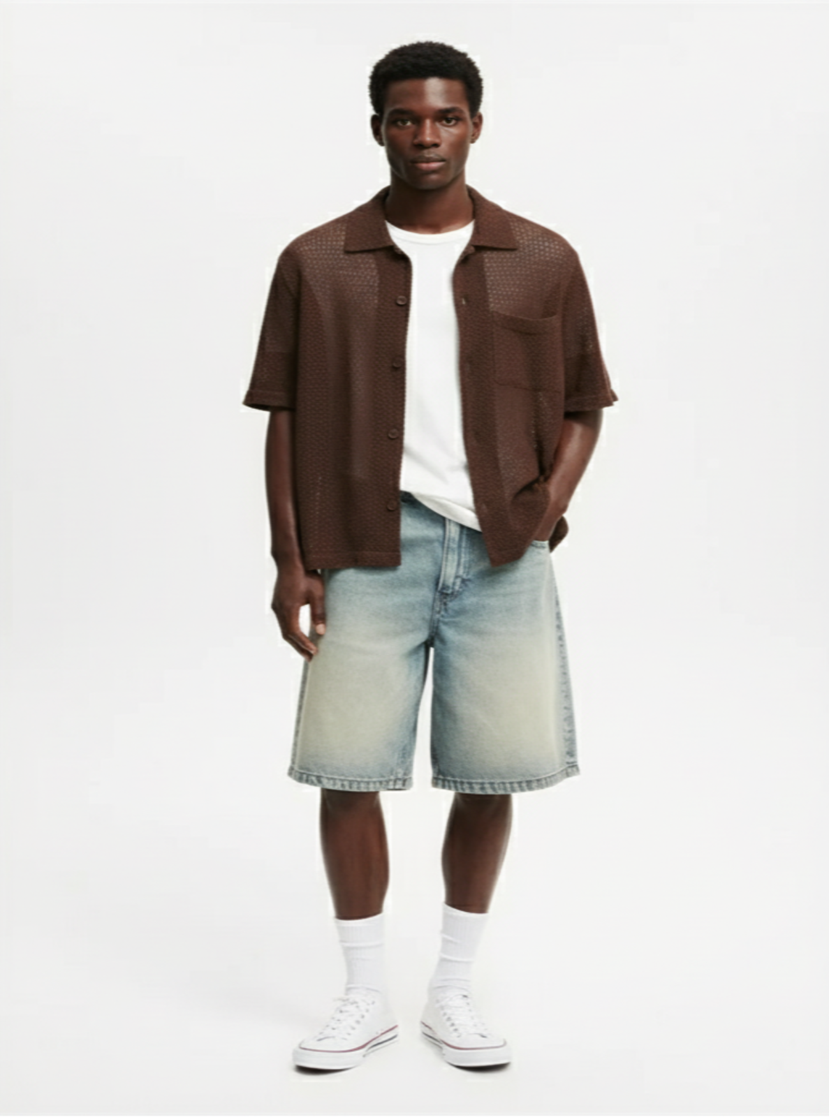Man wearing a brown shirt, white t-shirt, light blue shorts, and white sneakers on a white background