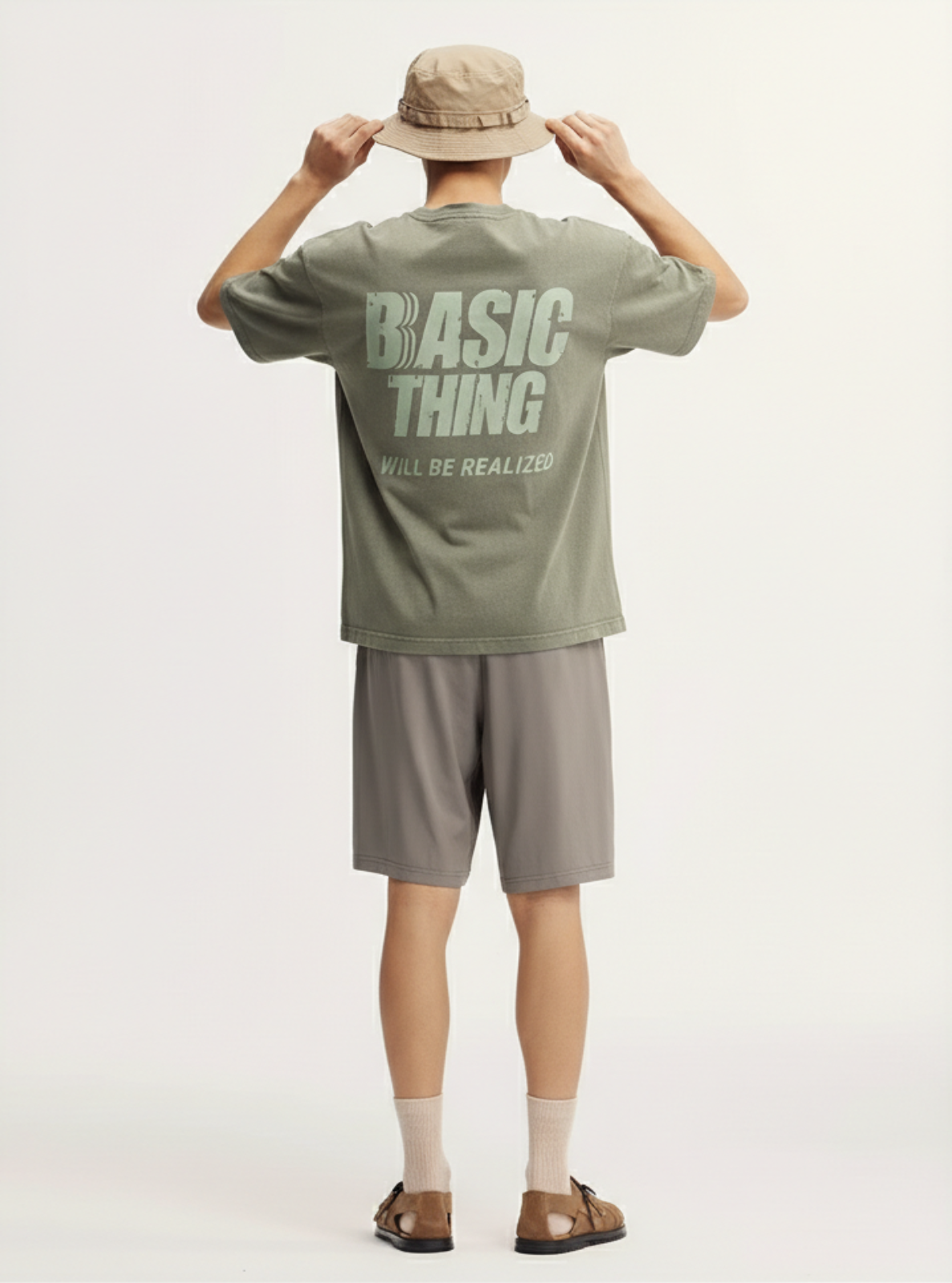 Person wearing a green t-shirt with text, beige shorts, and a beige cap on a white background