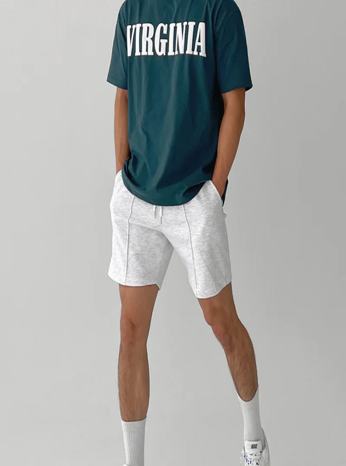 Person wearing a green 'Virginia' t-shirt and white shorts on a gray background