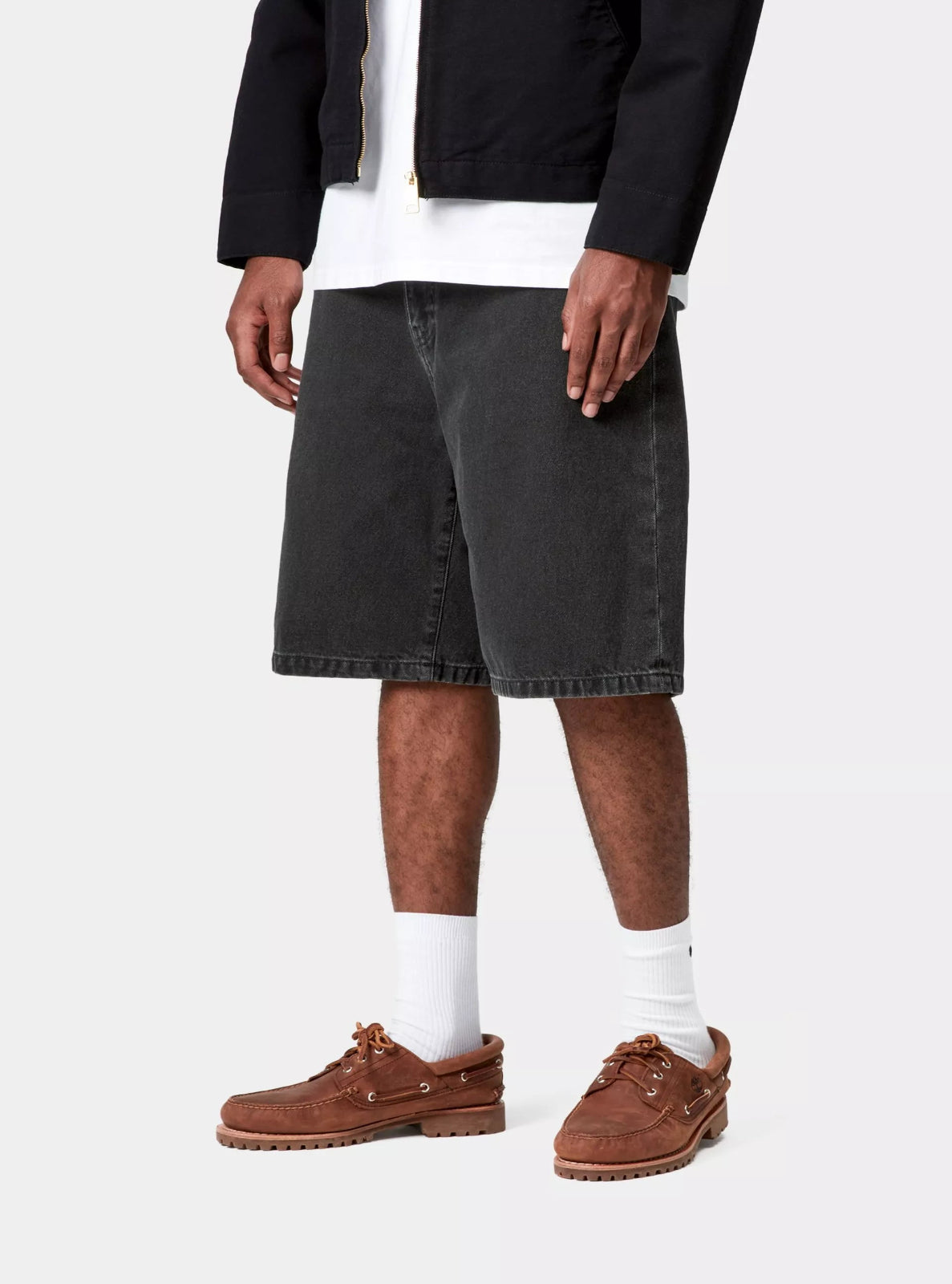 Person wearing black denim shorts, white socks, and brown shoes on a white background