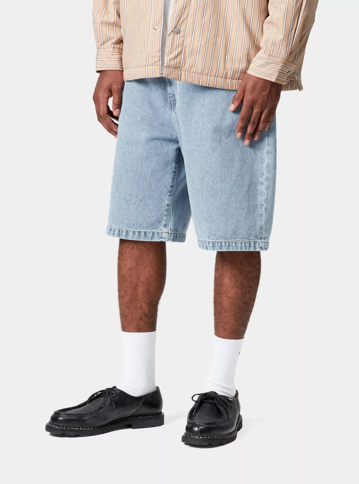 Person wearing light blue denim shorts, a beige jacket, white socks, and black shoes on a white background