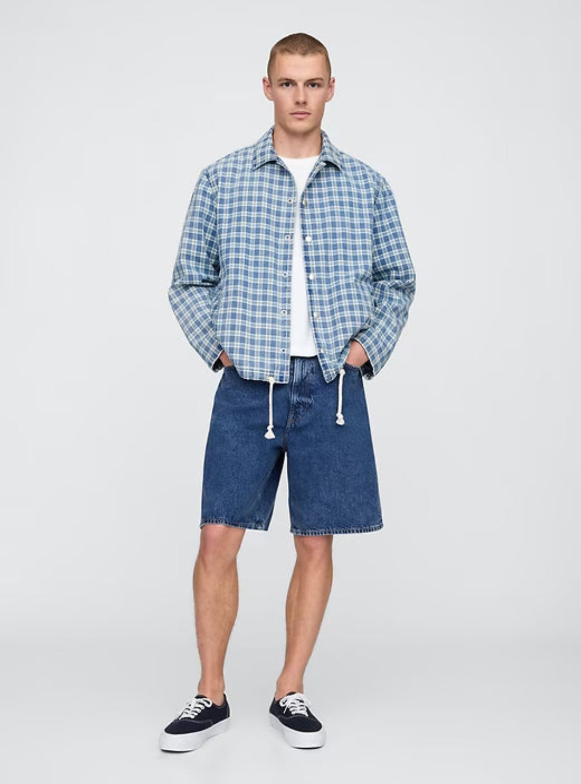 Man wearing a blue checkered shirt and denim shorts on a white background