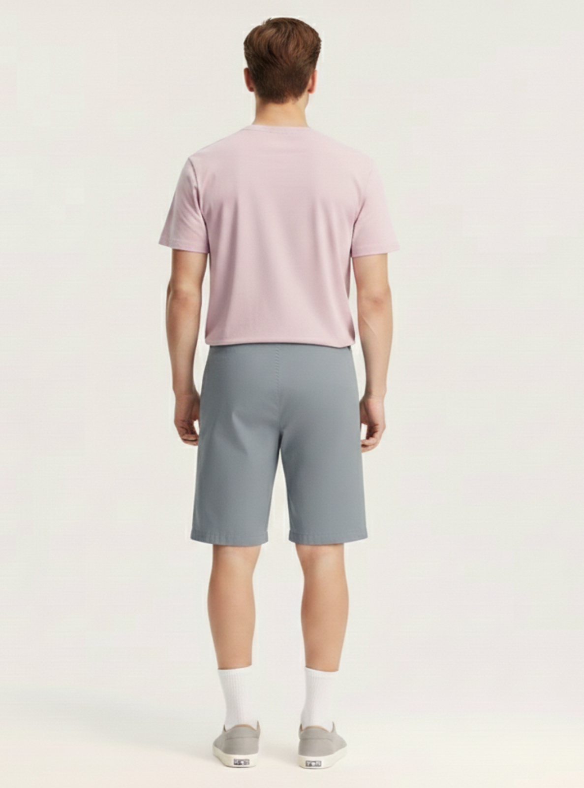 Man wearing a light pink t-shirt and gray shorts on a white background