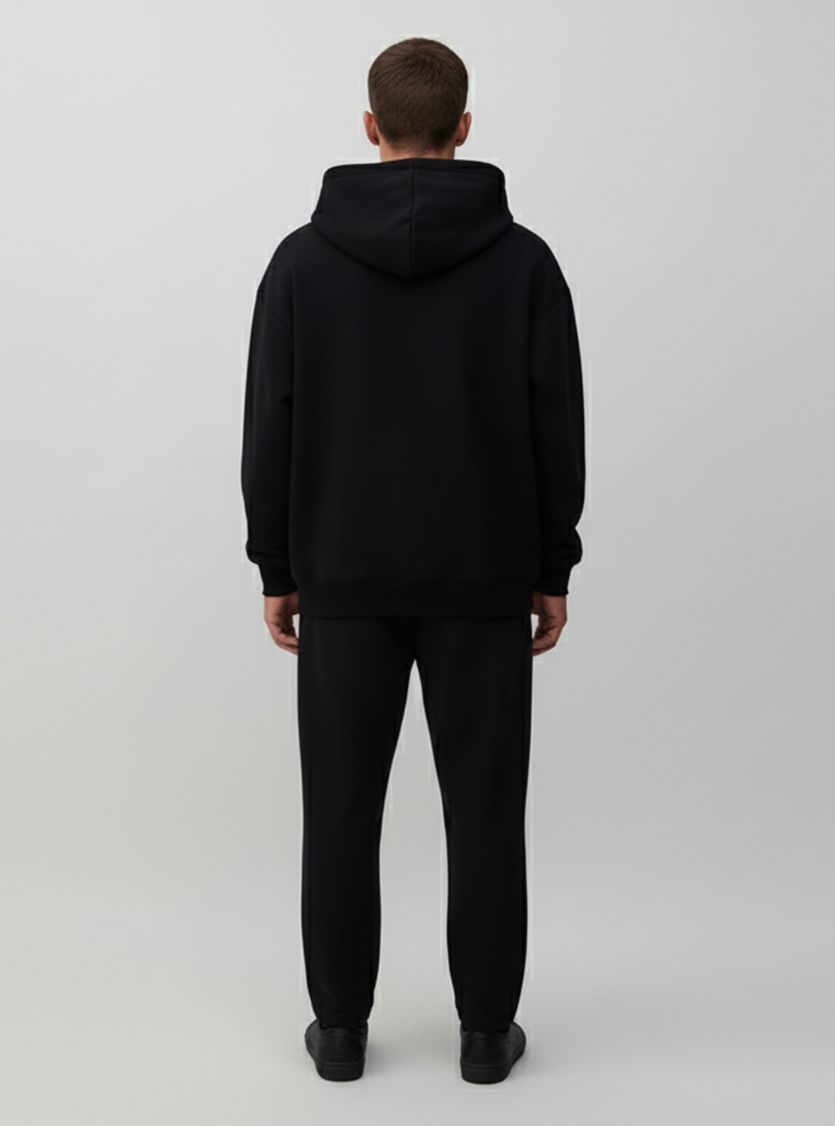 Person wearing a black hoodie and pants on a white background