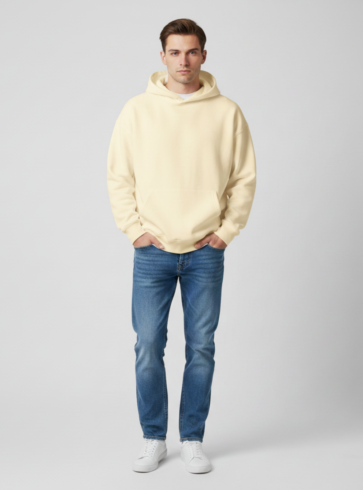Man wearing a light yellow hoodie and blue jeans on a gray background