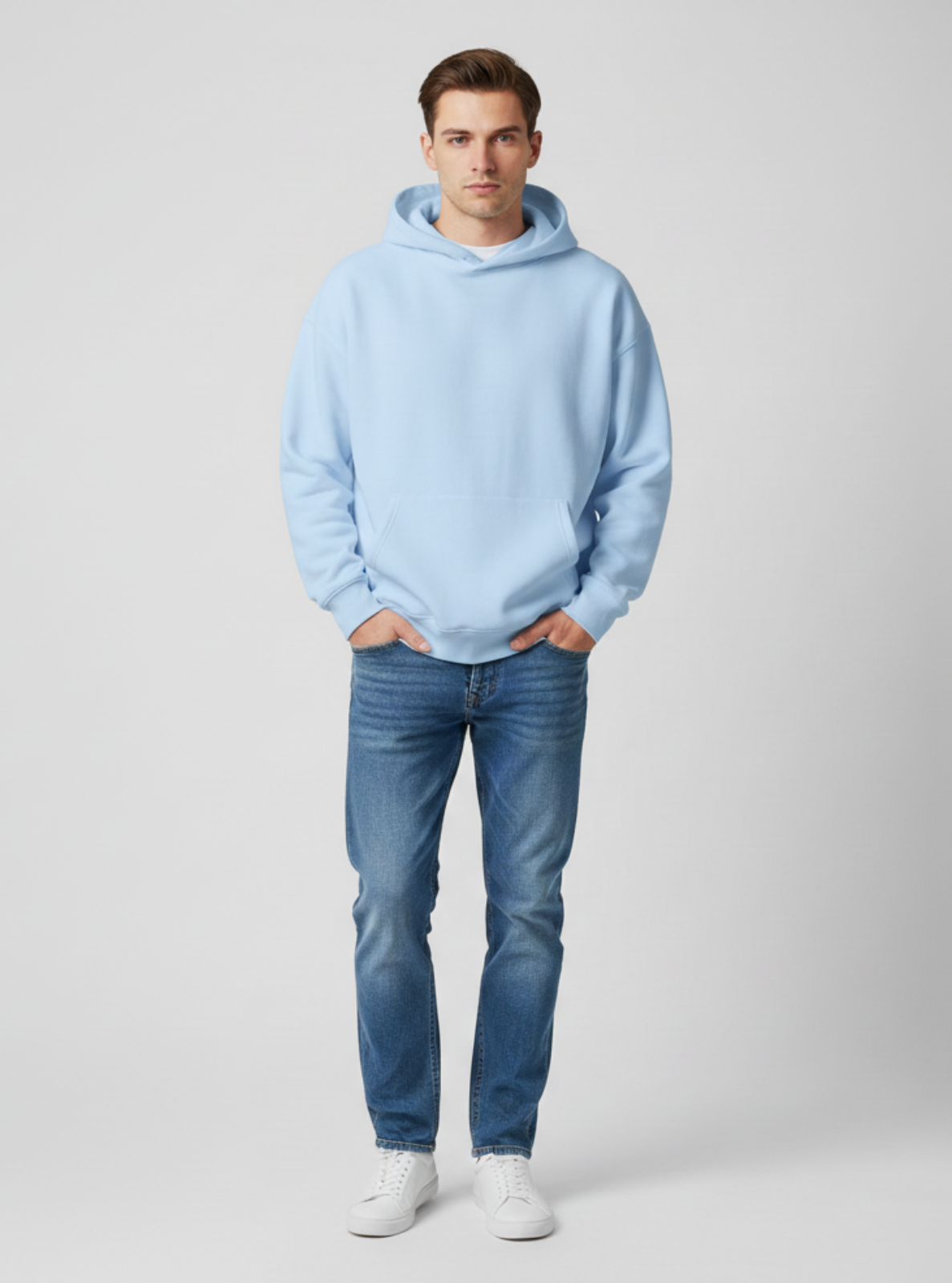 Man wearing a light blue hoodie and jeans on a plain background