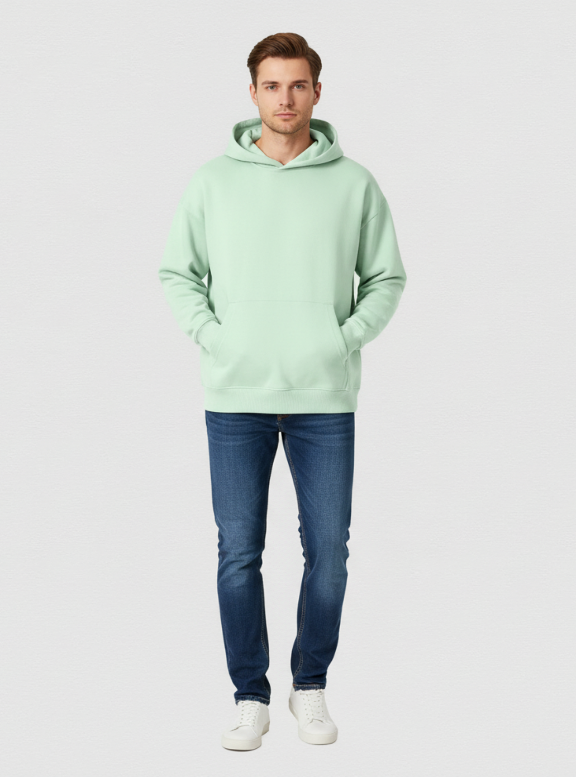 Man wearing a light green hoodie and blue jeans on a white background