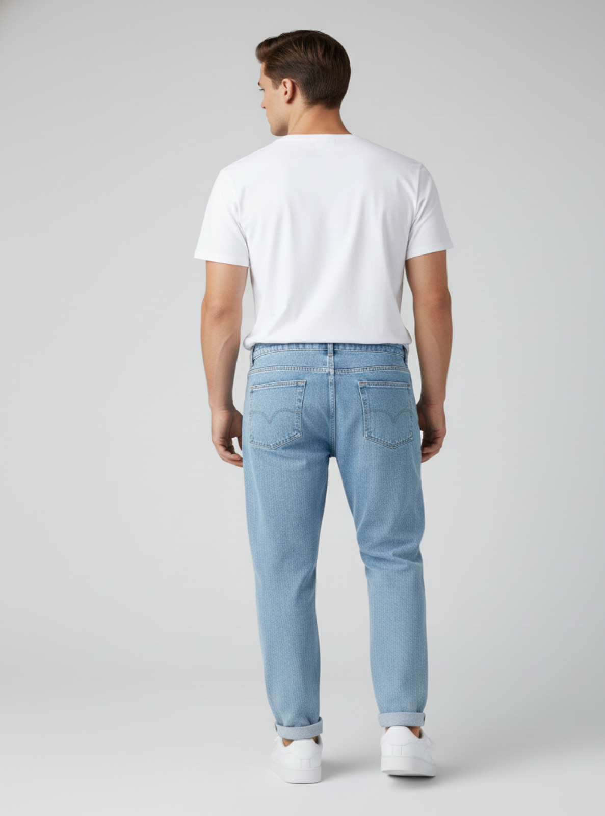 Man wearing a white t-shirt and light blue jeans on a gray background