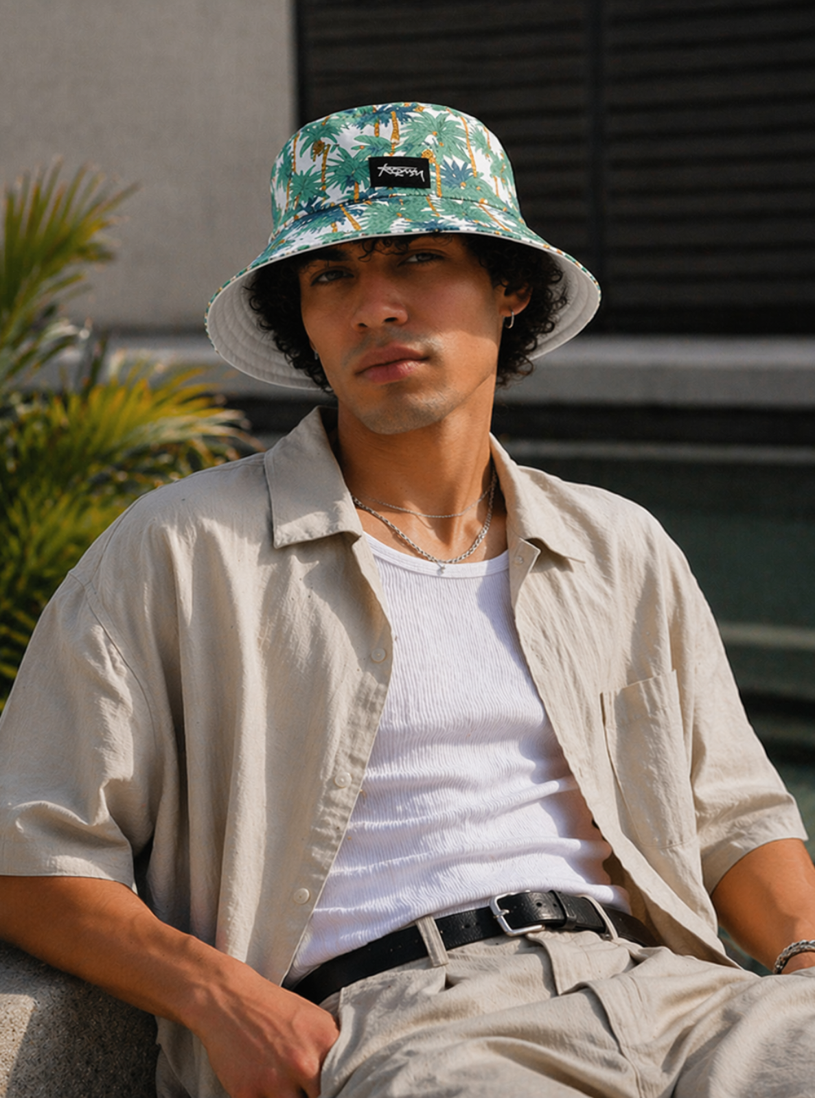 Man wearing a floral bucket hat and beige shirt sitting outdoors.