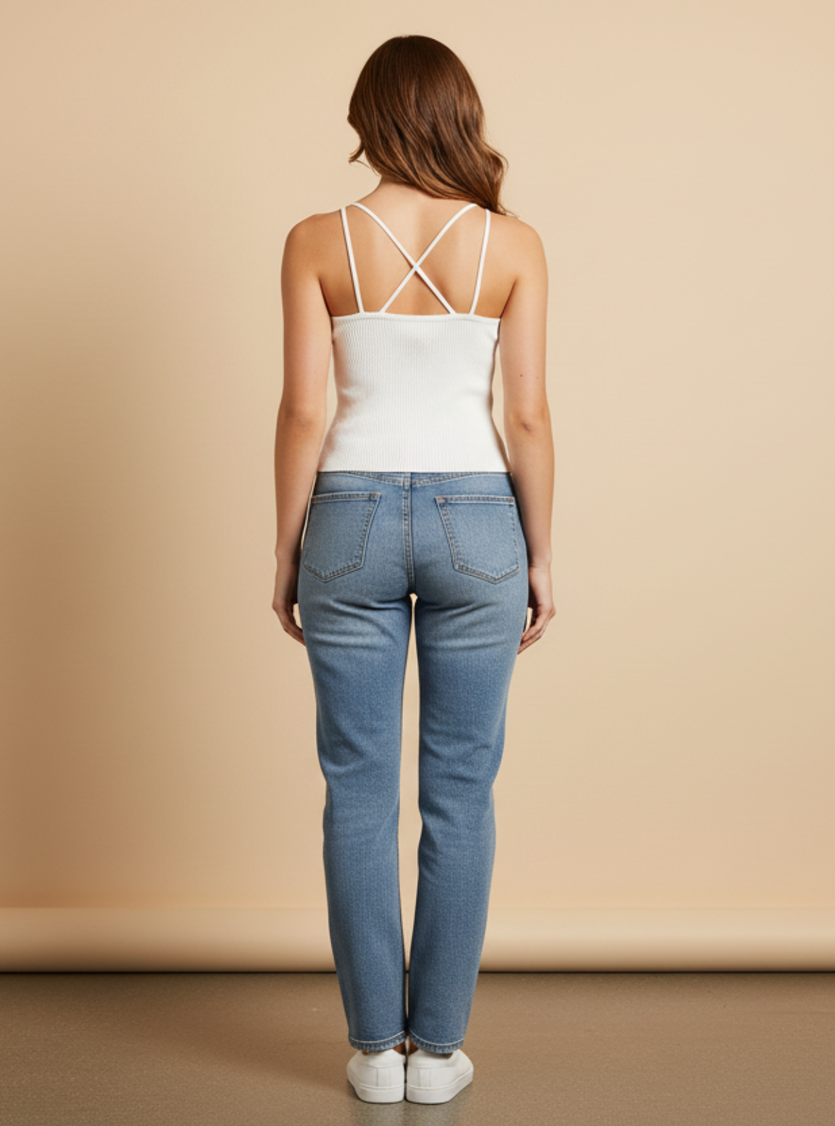 Woman wearing a white top and blue jeans against a beige background