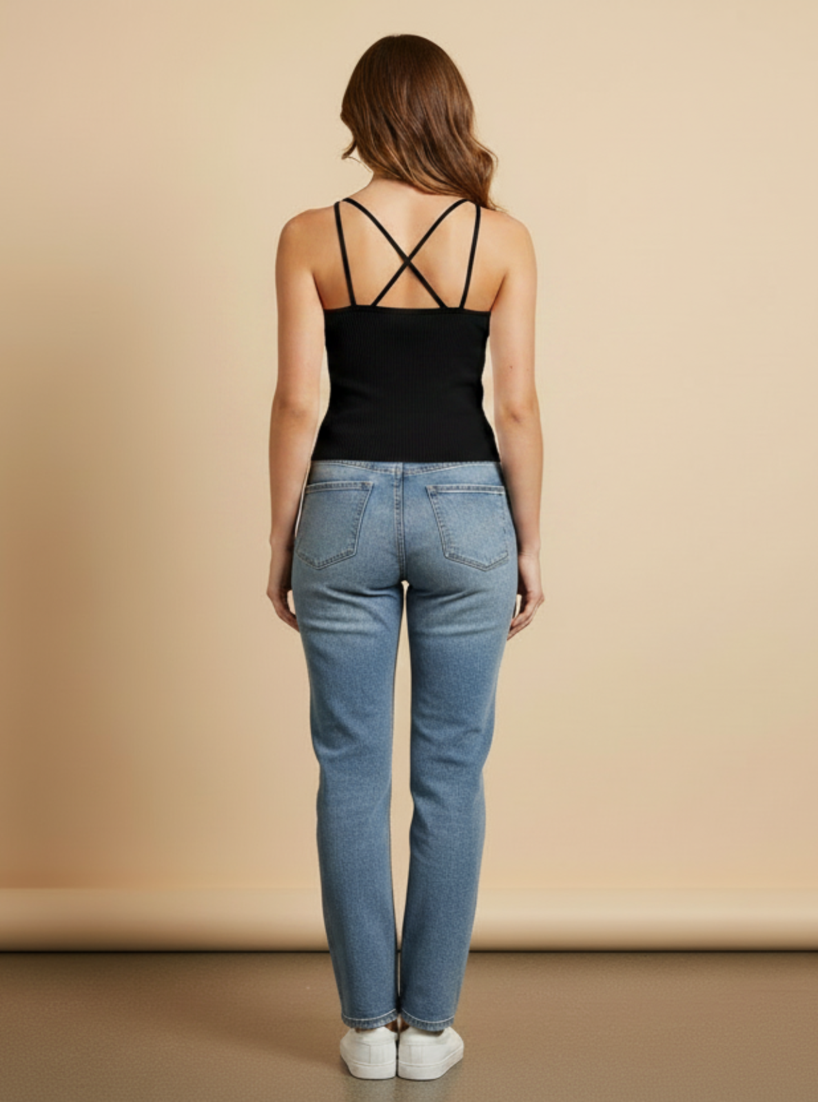 Woman wearing a black tank top and blue jeans against a beige background