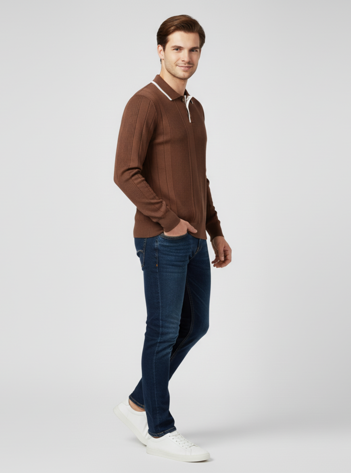Man wearing a brown sweater, blue jeans, and white shoes on a light gray background