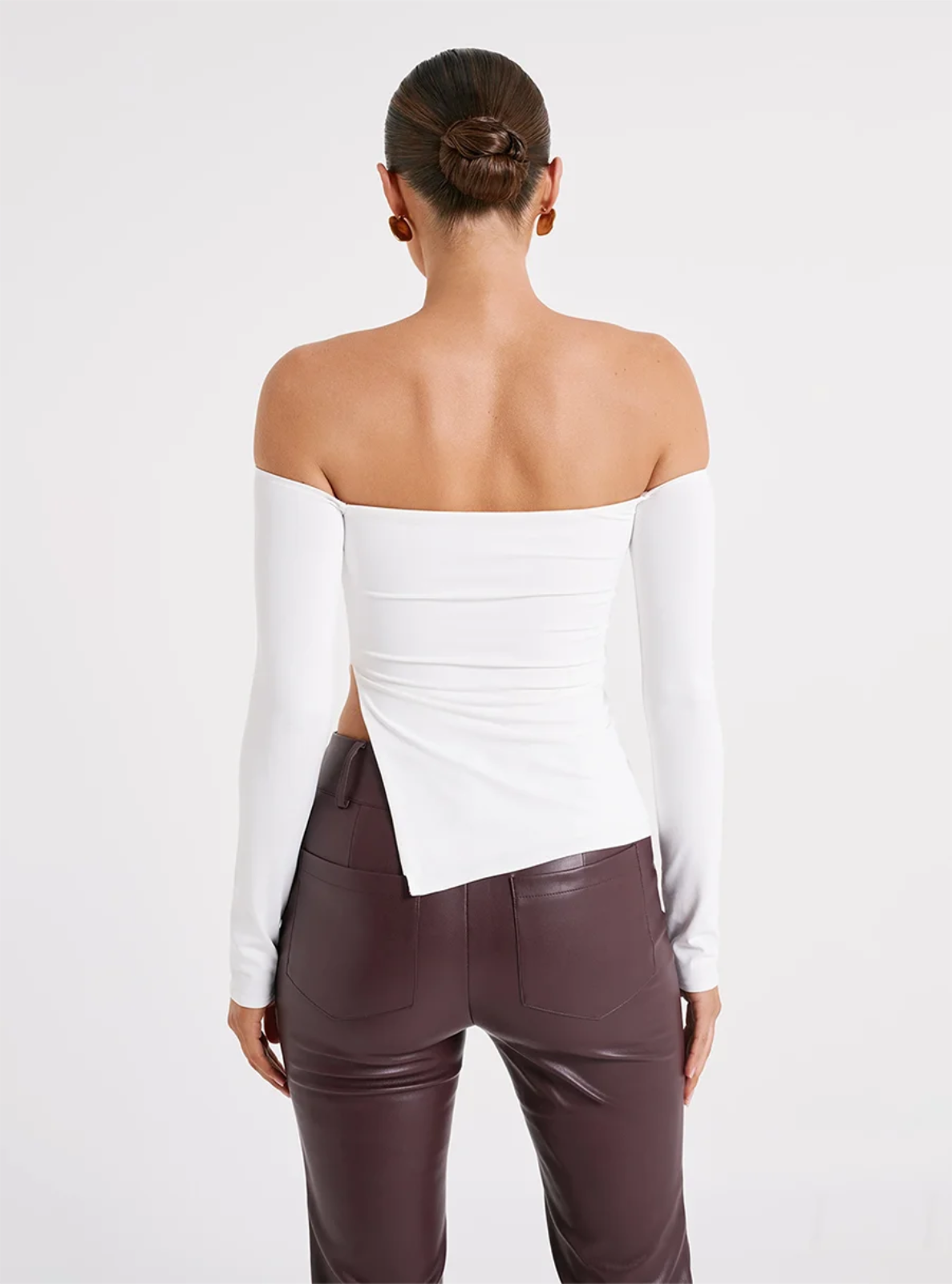 Person wearing a white off-shoulder top and maroon pants on a light gray background