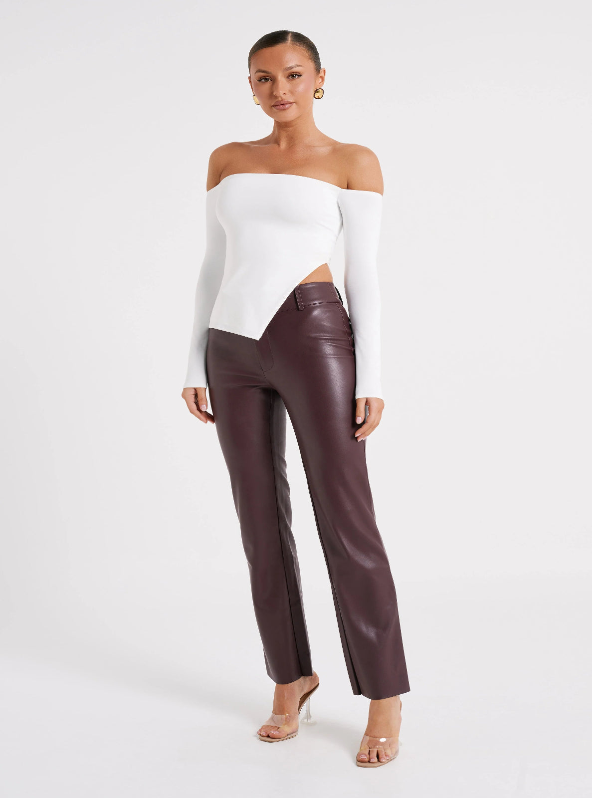 Woman wearing a white off-shoulder top and brown leather pants on a white background