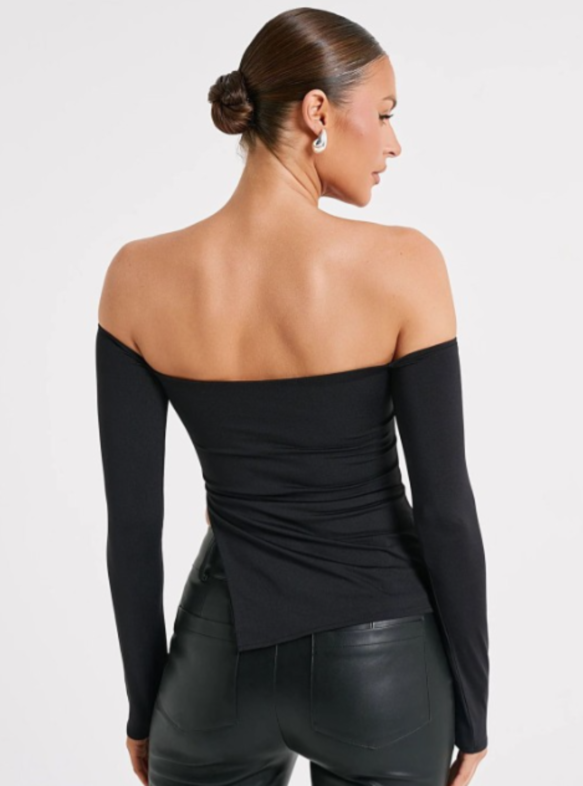Woman wearing a black off-shoulder top and leather pants on a white background