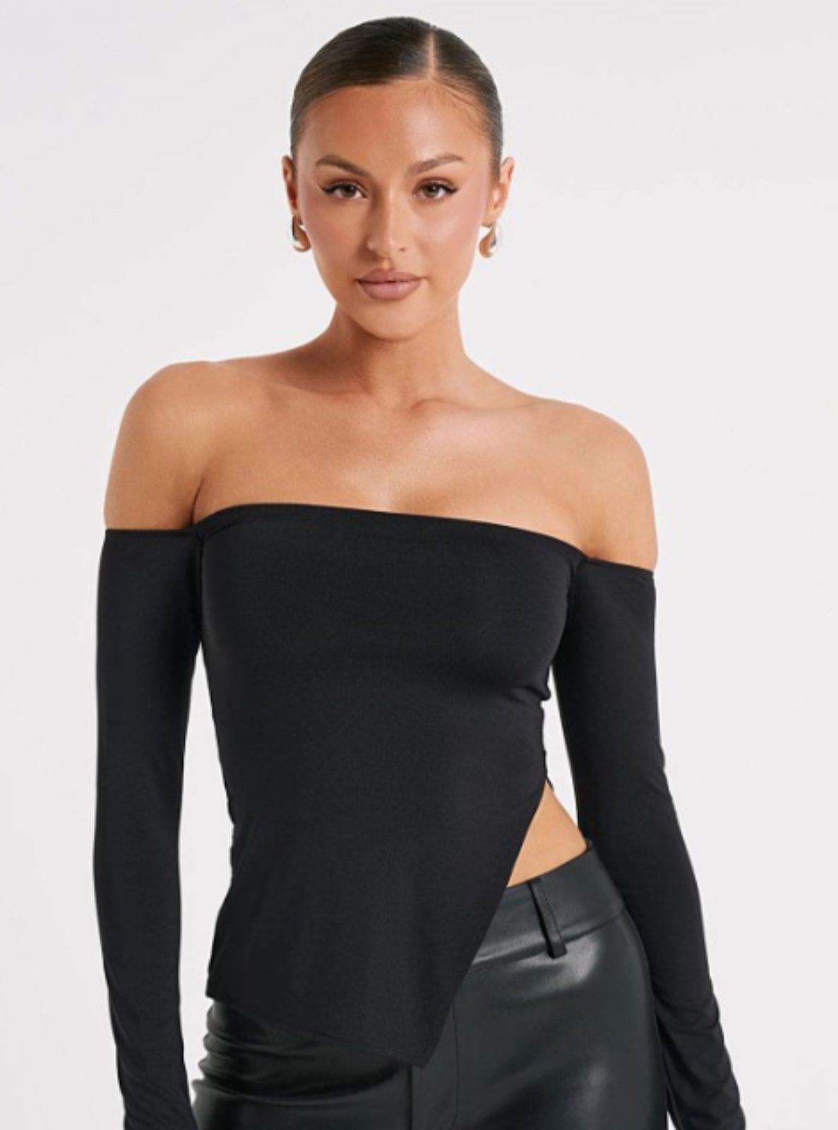 Woman wearing a black off-shoulder top and black leather pants on a white background