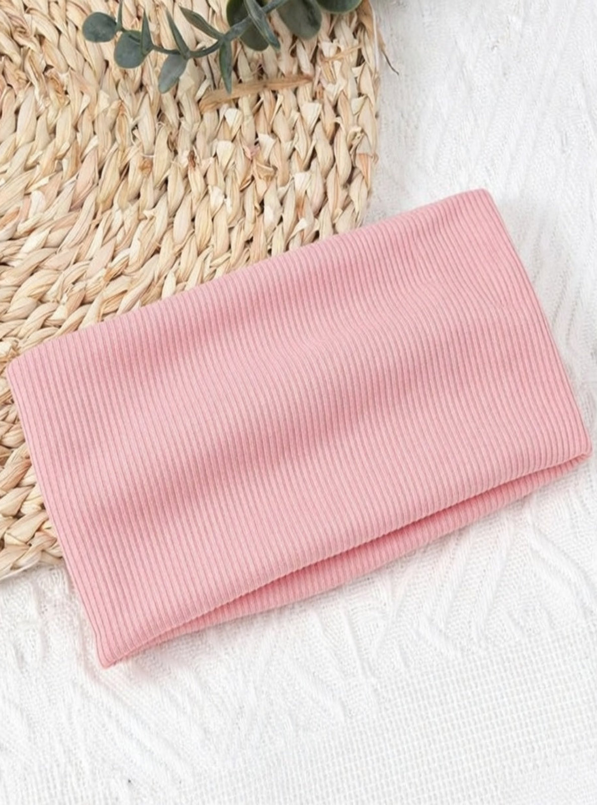 Folded pink fabric on a textured surface with a woven mat and green leaves.