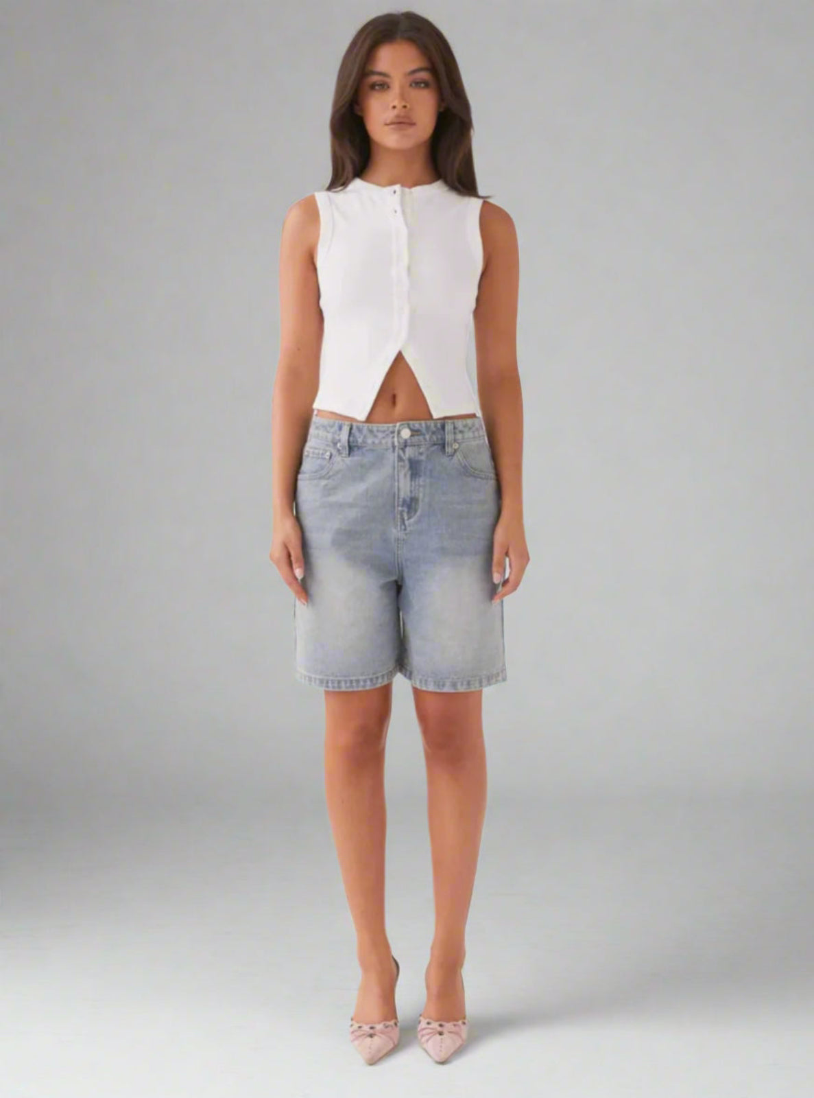 Woman wearing a white sleeveless top and denim shorts on a gray background