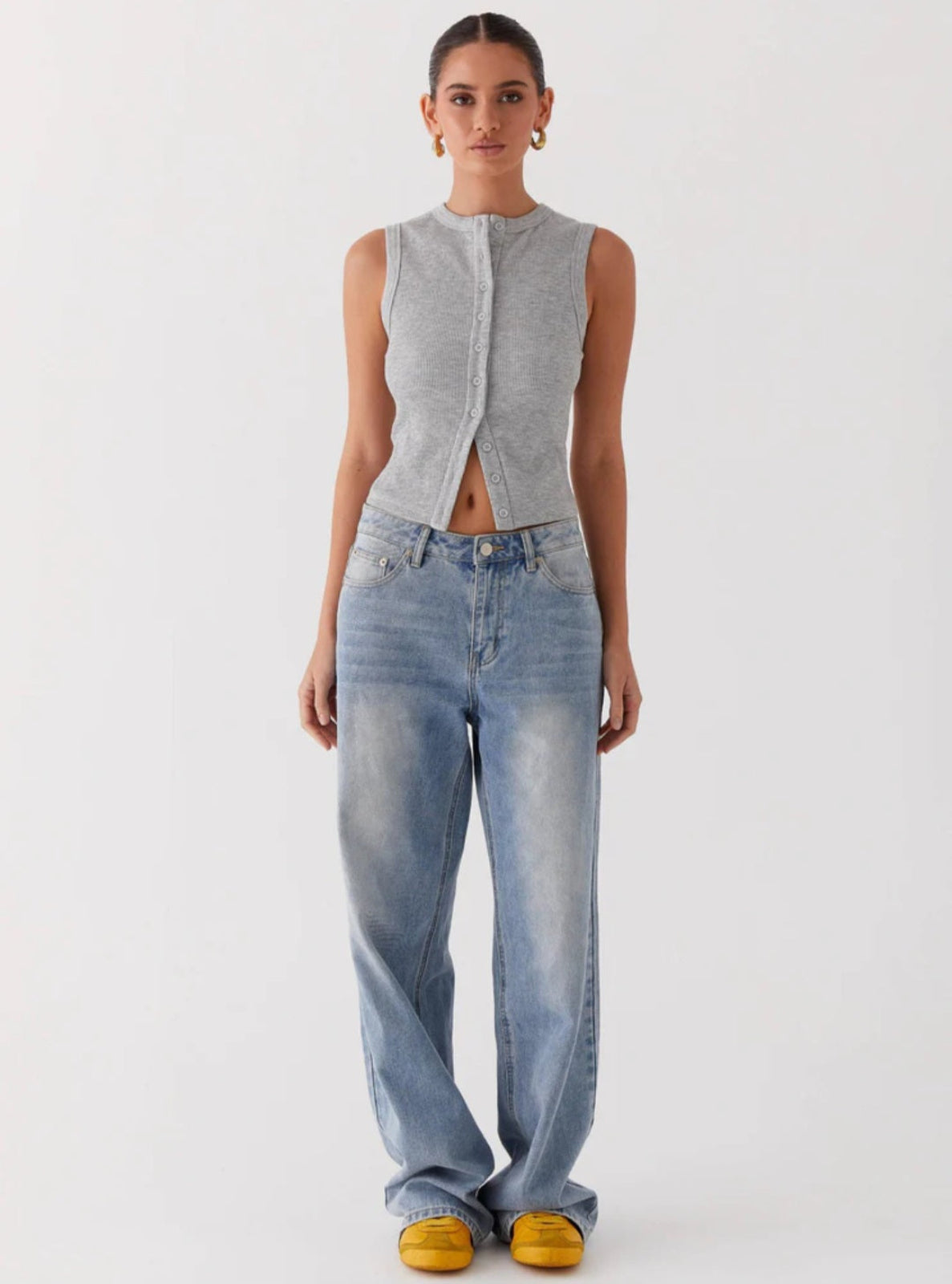 Woman wearing a gray sleeveless top and light blue jeans on a white background