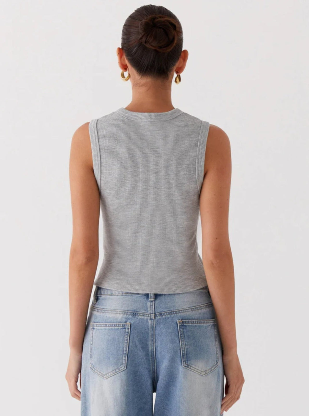 Person wearing a gray sleeveless top and blue jeans on a plain background