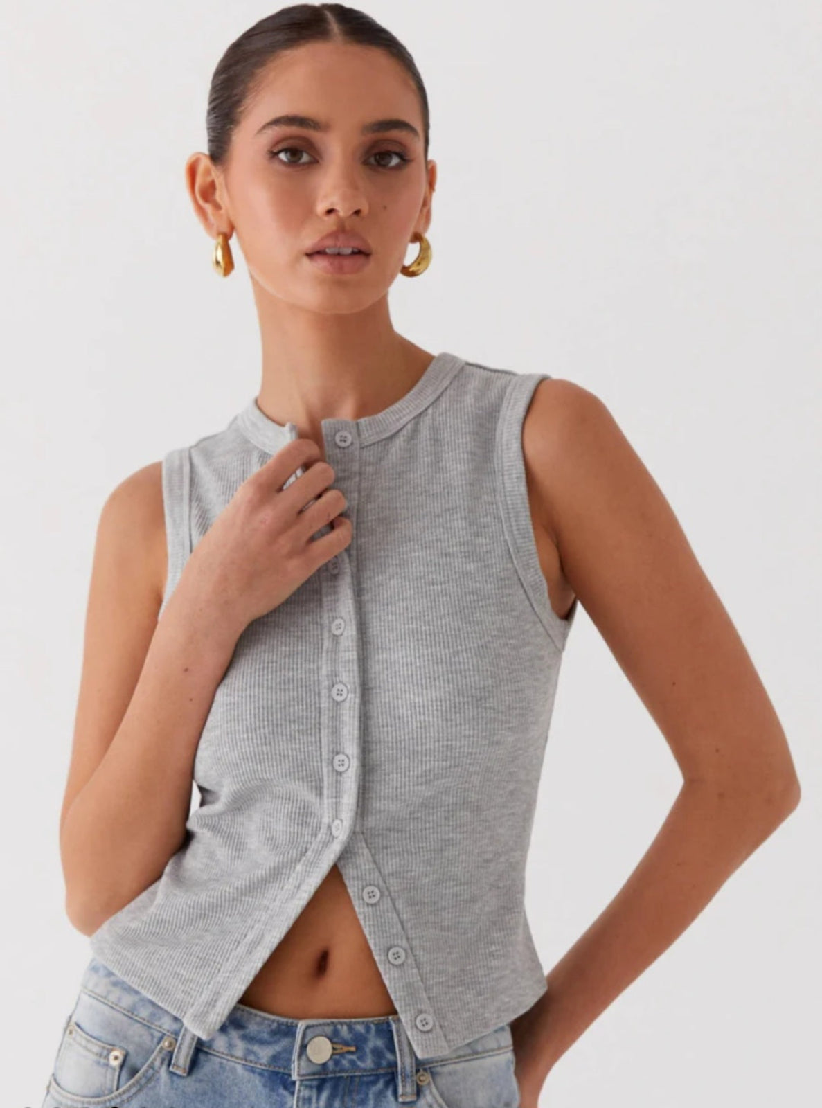 Woman wearing a gray sleeveless button-up top with a white shirt underneath on a light gray background