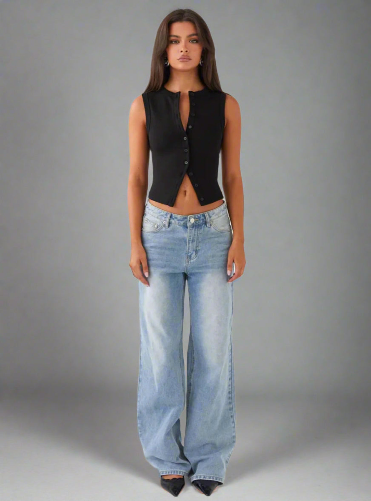 Woman wearing a black sleeveless top and light blue jeans against a gray background
